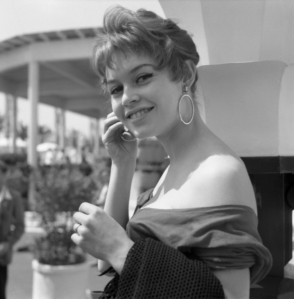 La jeune Brigitte Bardot, mannequin, chanteuse et actrice française, au Festival de Cannes, vêtue d'un chemisier dos nu et de grandes boucles d'oreilles rondes, Cannes, 1955 I Source : Getty Images