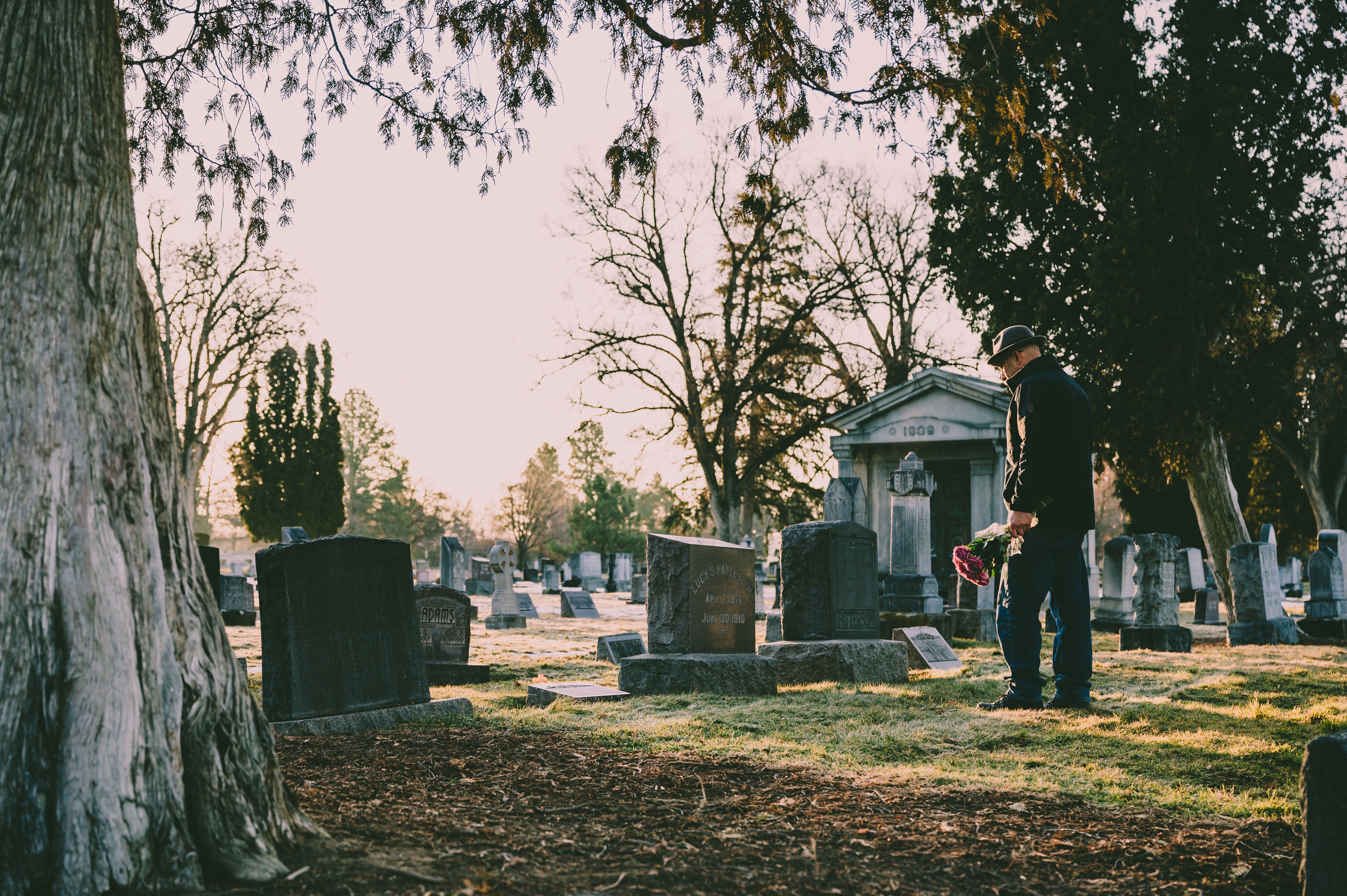 Homme debout dans une veste noire devant une tombe, des fleurs à la main. | Photo : Pexels