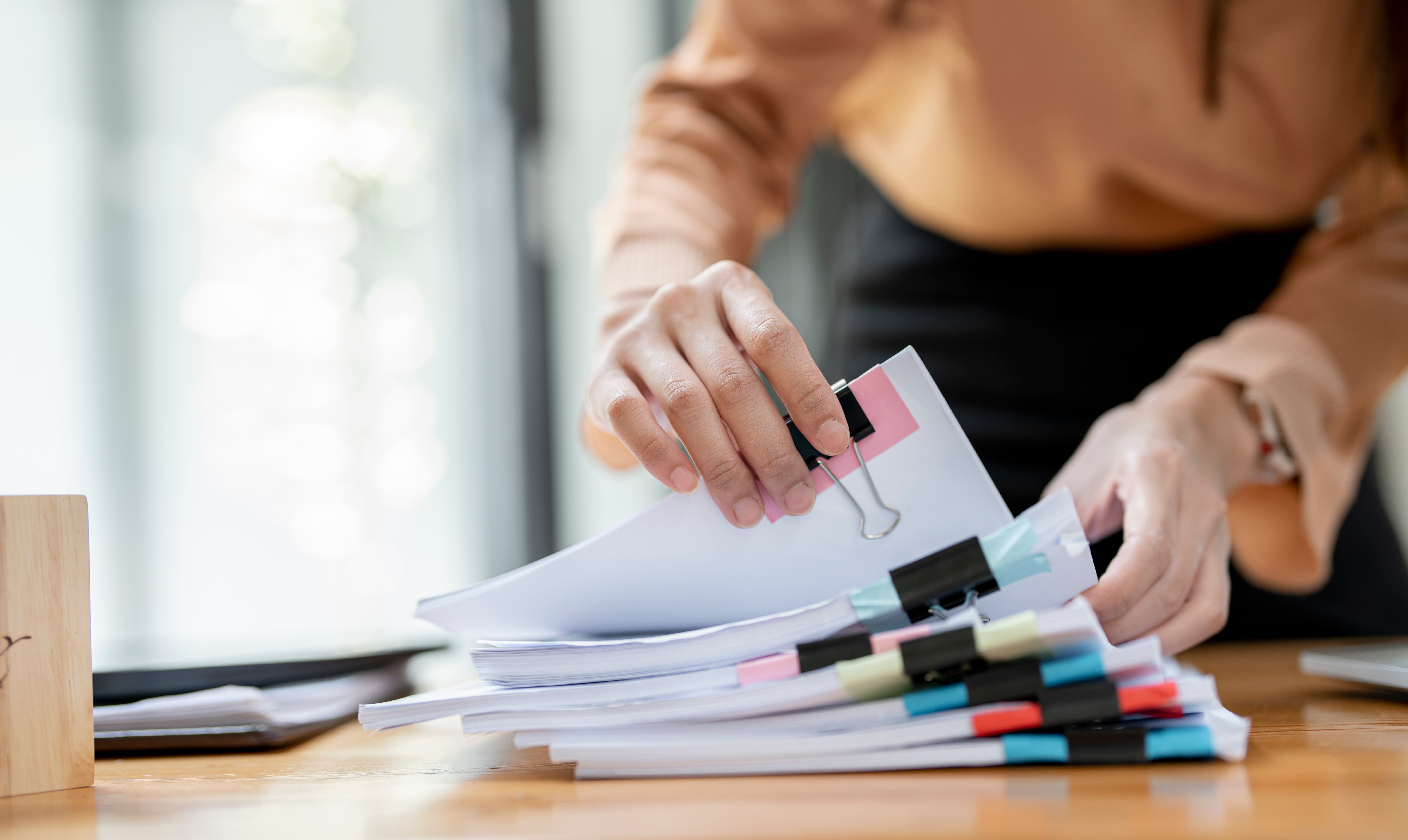 Manos de empresaria trabajando en pilas de archivos de papel para buscar documentos | Fuente: Shutterstock.com