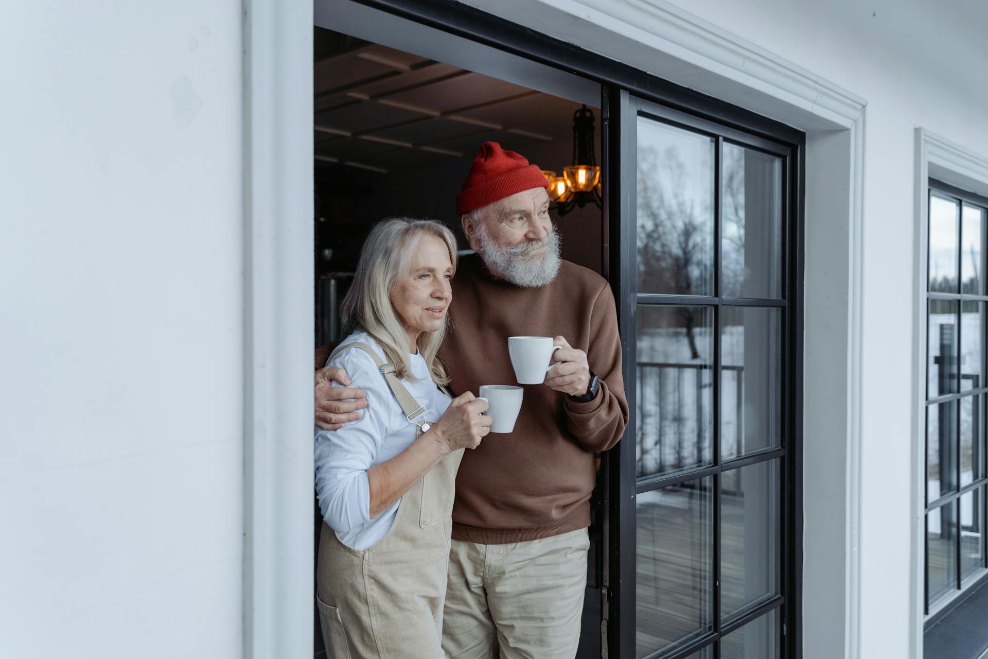 Un couple âgé se tenant sur le pas d'une porte, chacun tenant une tasse | Source : Pexels