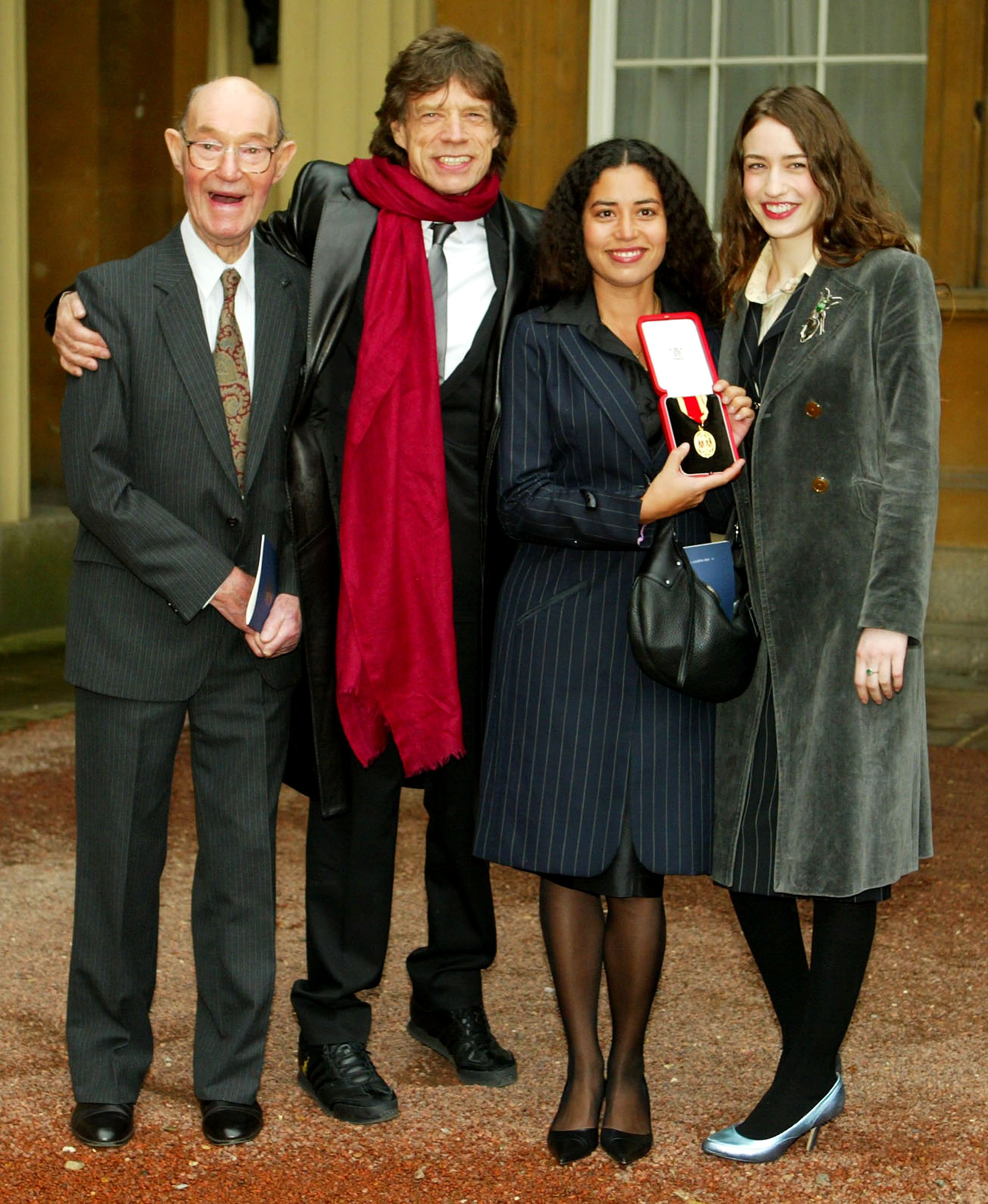 Le père Joe avec le rockeur vétéran Mick Jagger et ses filles Karis et Elizabeth au Buckingham Palace le 12 décembre 2003 à Londres. / Source : Getty Images