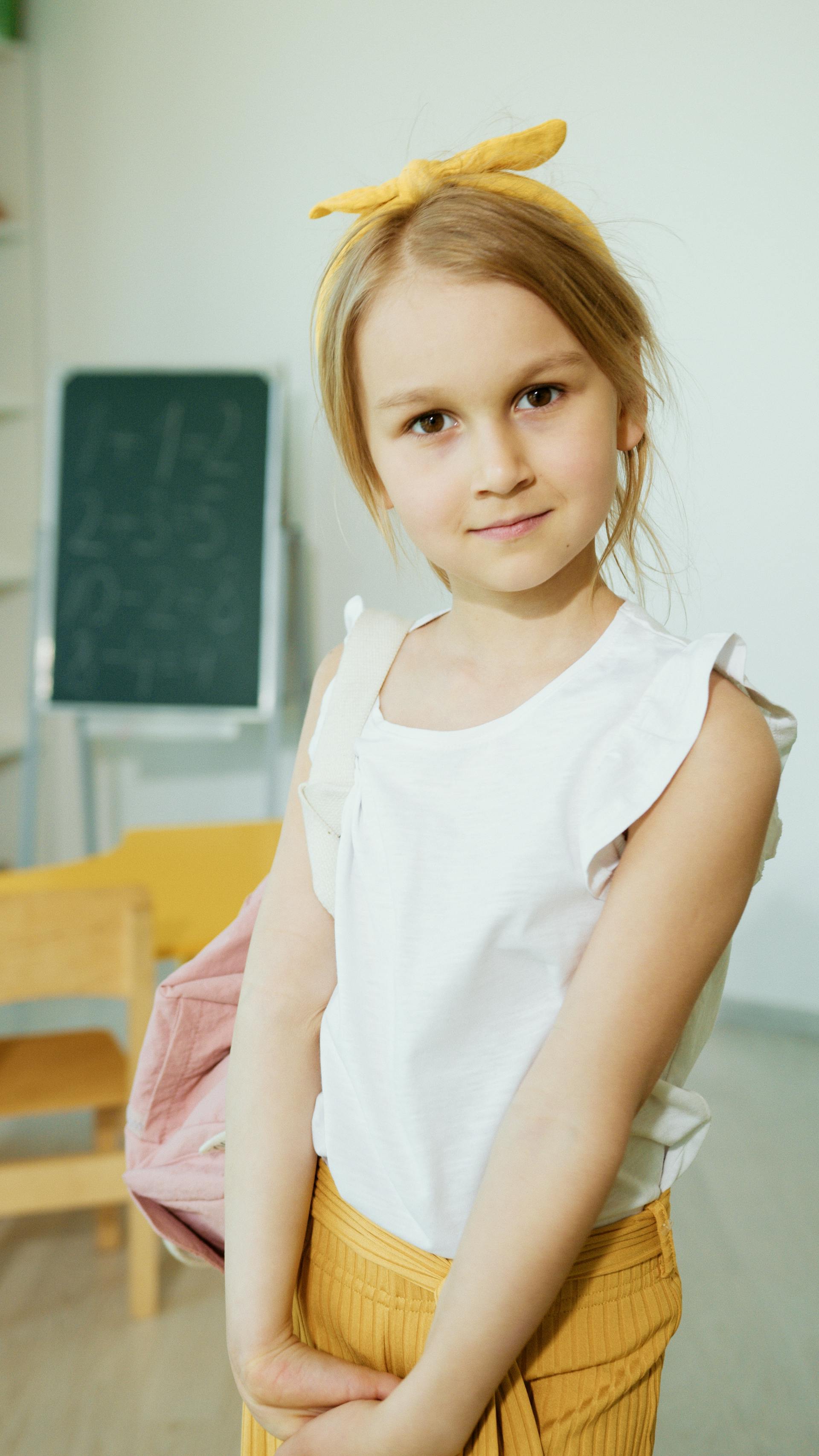 Une petite fille vêtue d'une blouse blanche sans manches sourit dans une chambre | Source : Pexels