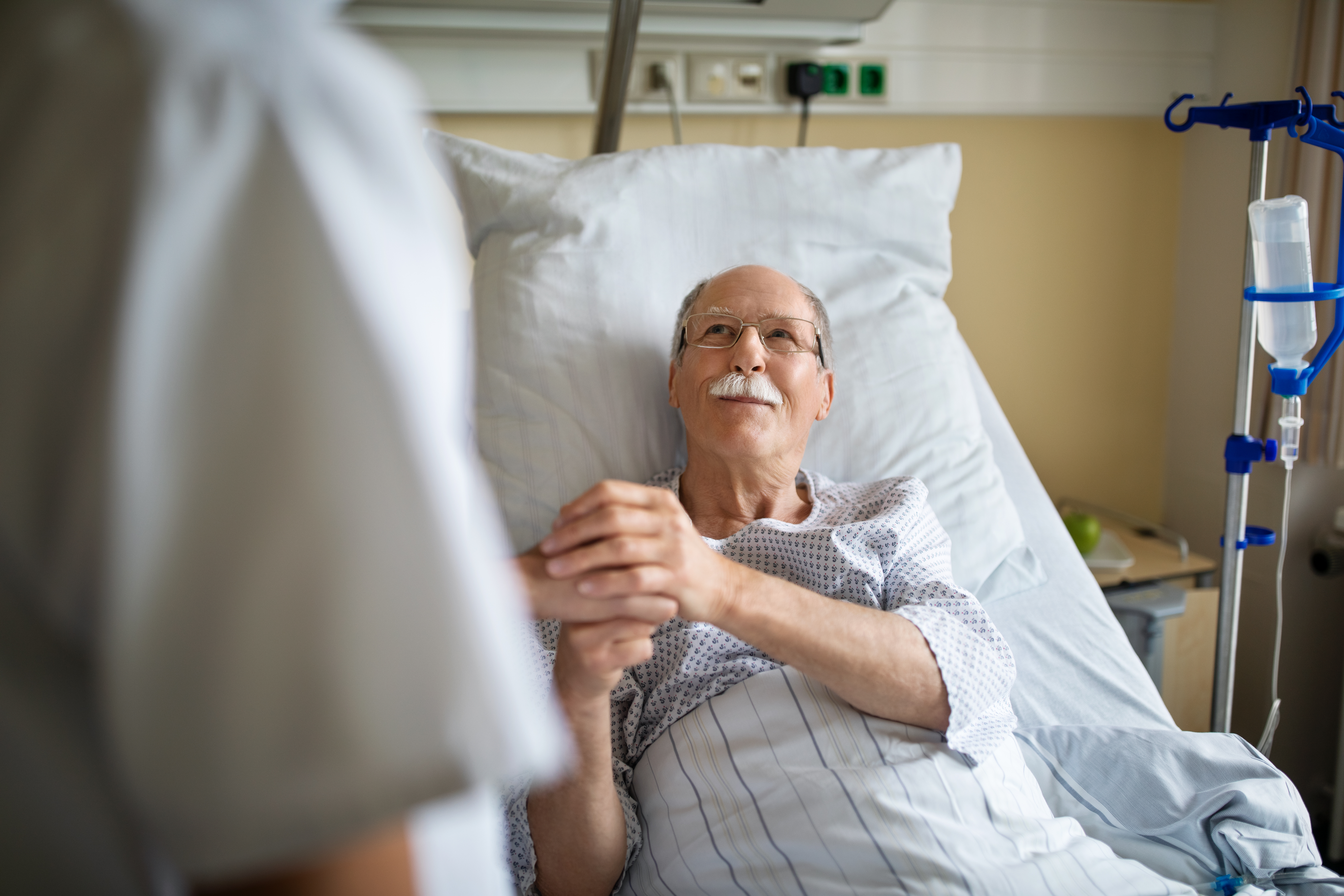 Un homme âgé tient la main d'une infirmière dans une chambre d'hôpital | Source : Getty Images