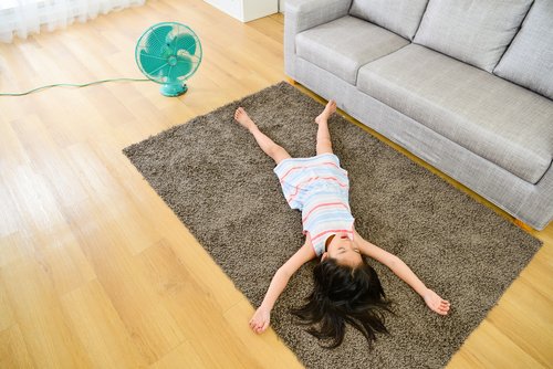 Une fillette couchée sur un tapis avec le ventilateur allumé | Photo : Shutterstock.