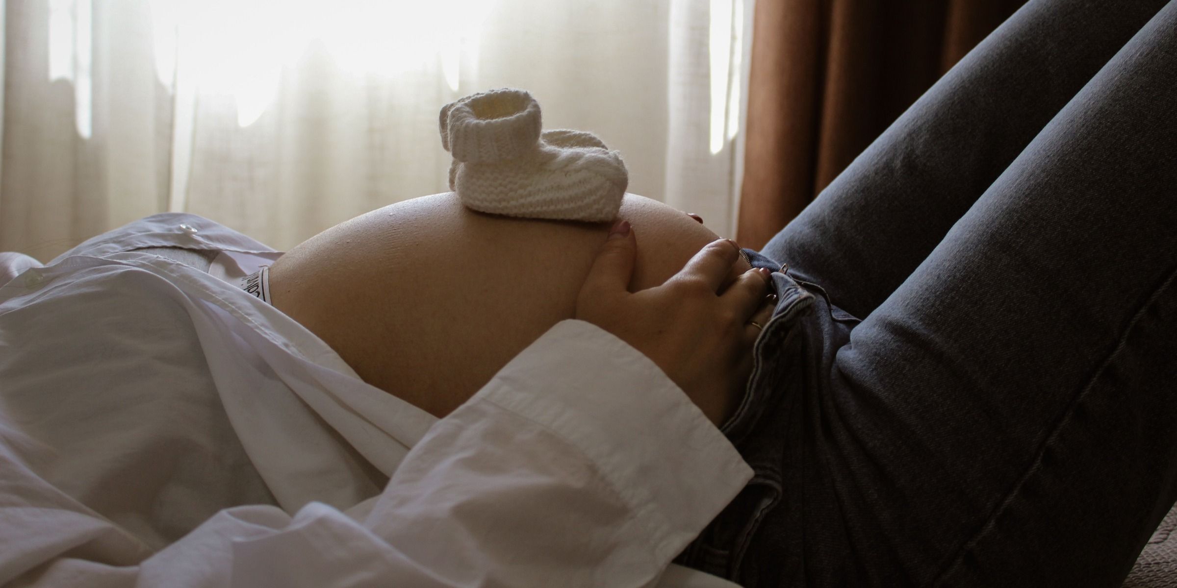 Une future maman se repose avec des chaussons de bébé posés sur son ventre | Source : Pexels