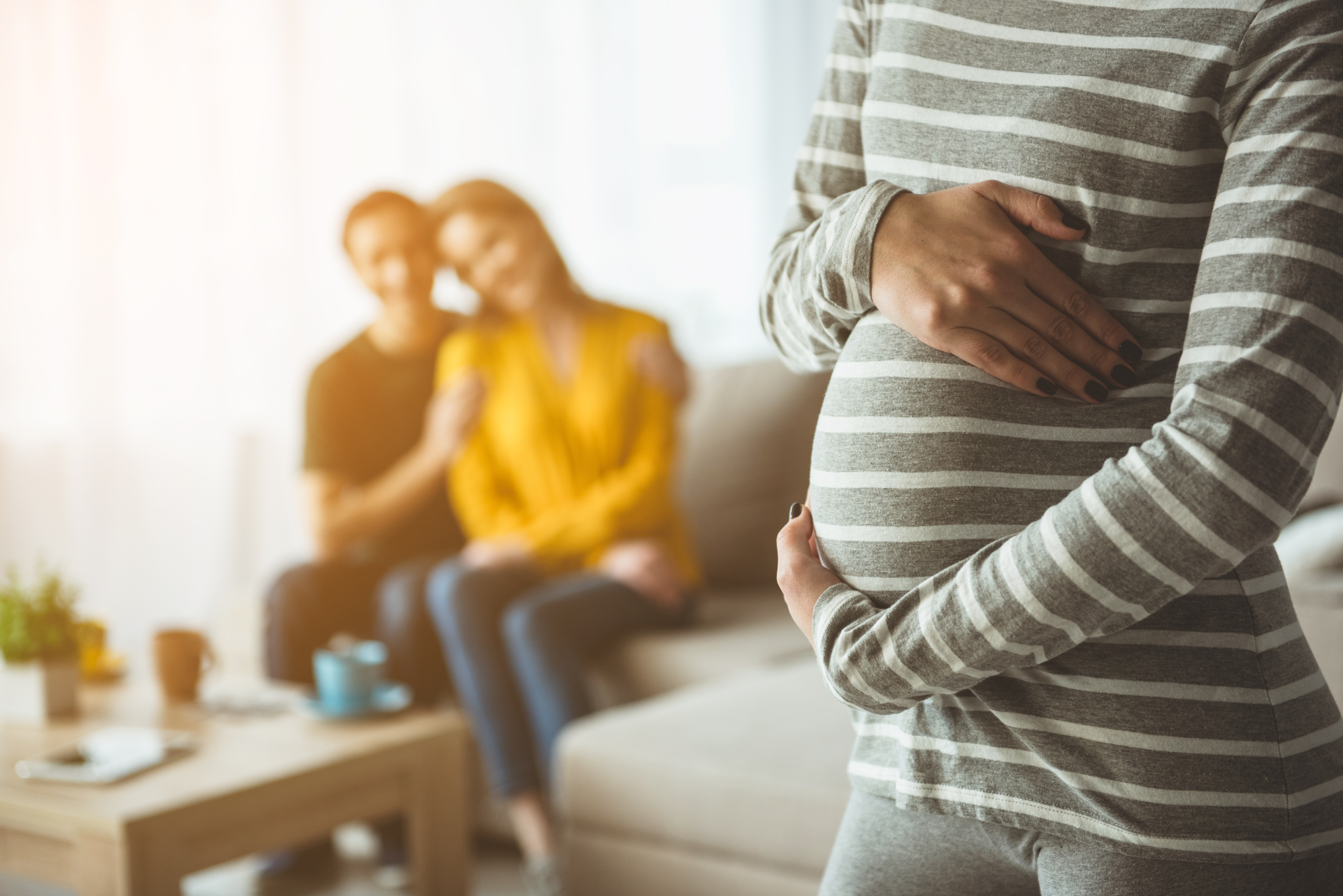 Une femme enceinte touchant son ventre avec un couple heureux à l'arrière-plan. | Source : Shutterstock