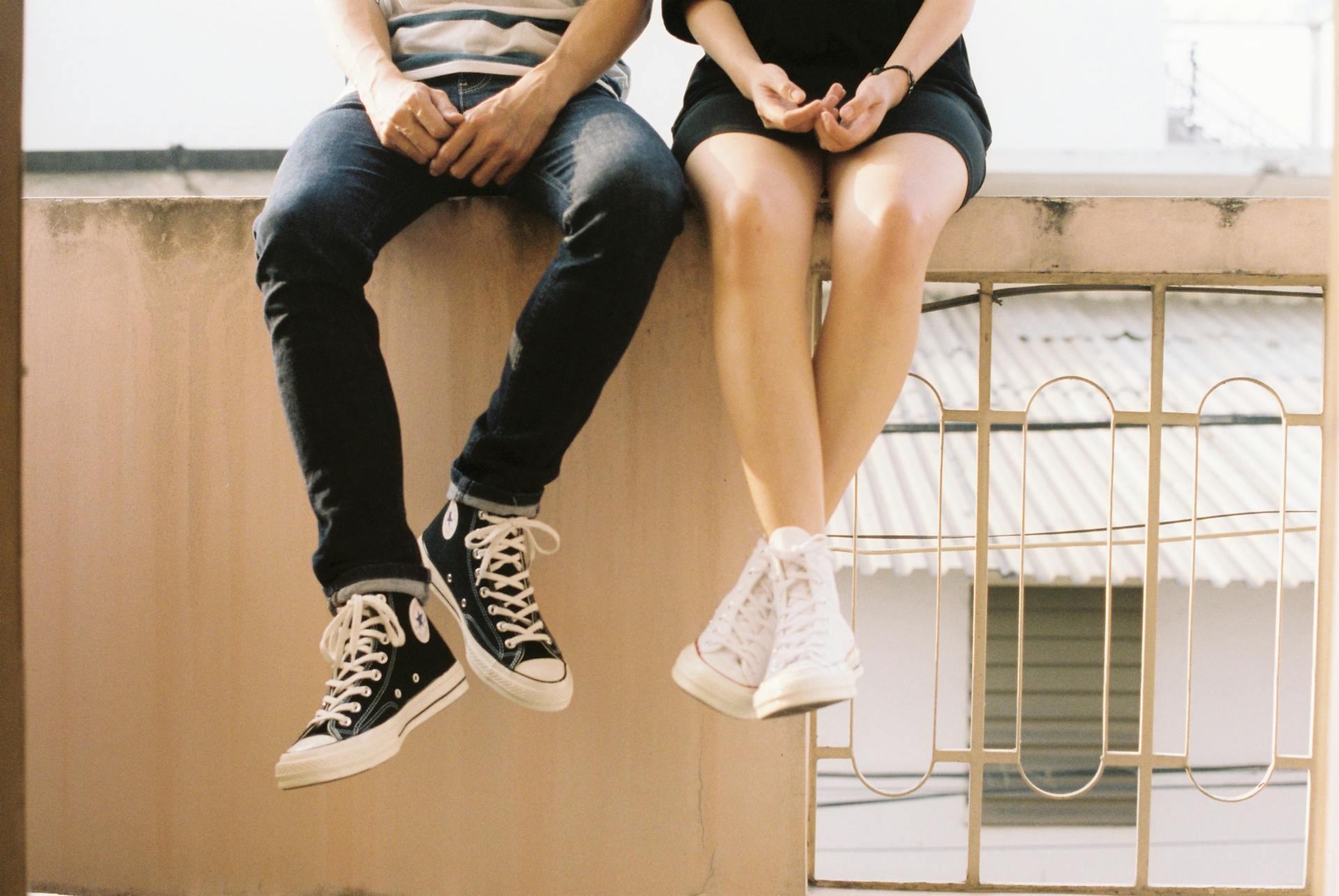 Jeune couple assis sur un mur portant des converses | Source : Pexels