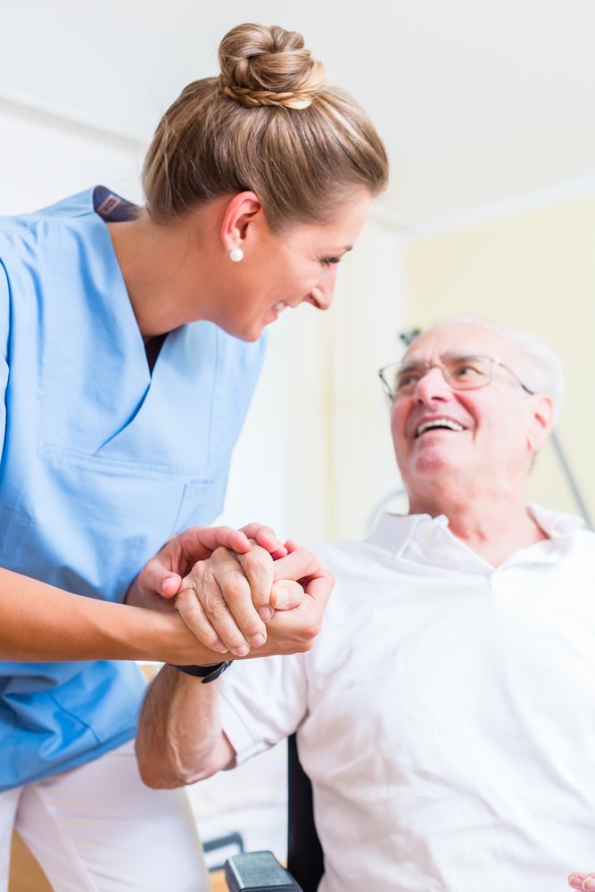 Une infirmière tenant la main d'un homme agé dans une maison de retraite. | Shutterstock