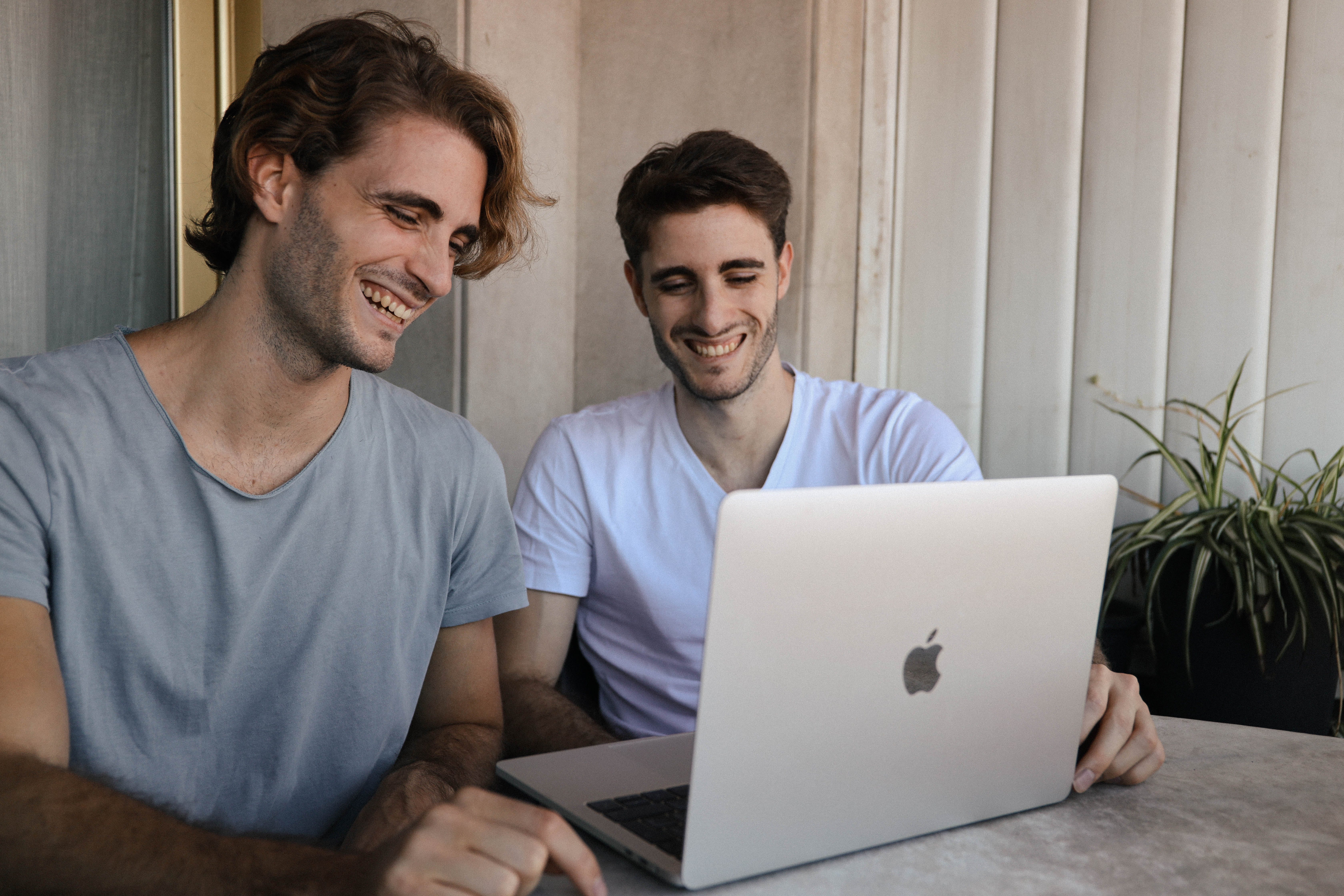 Deux jeunes hommes rient en utilisant un ordinateur portable | Source : Pexels