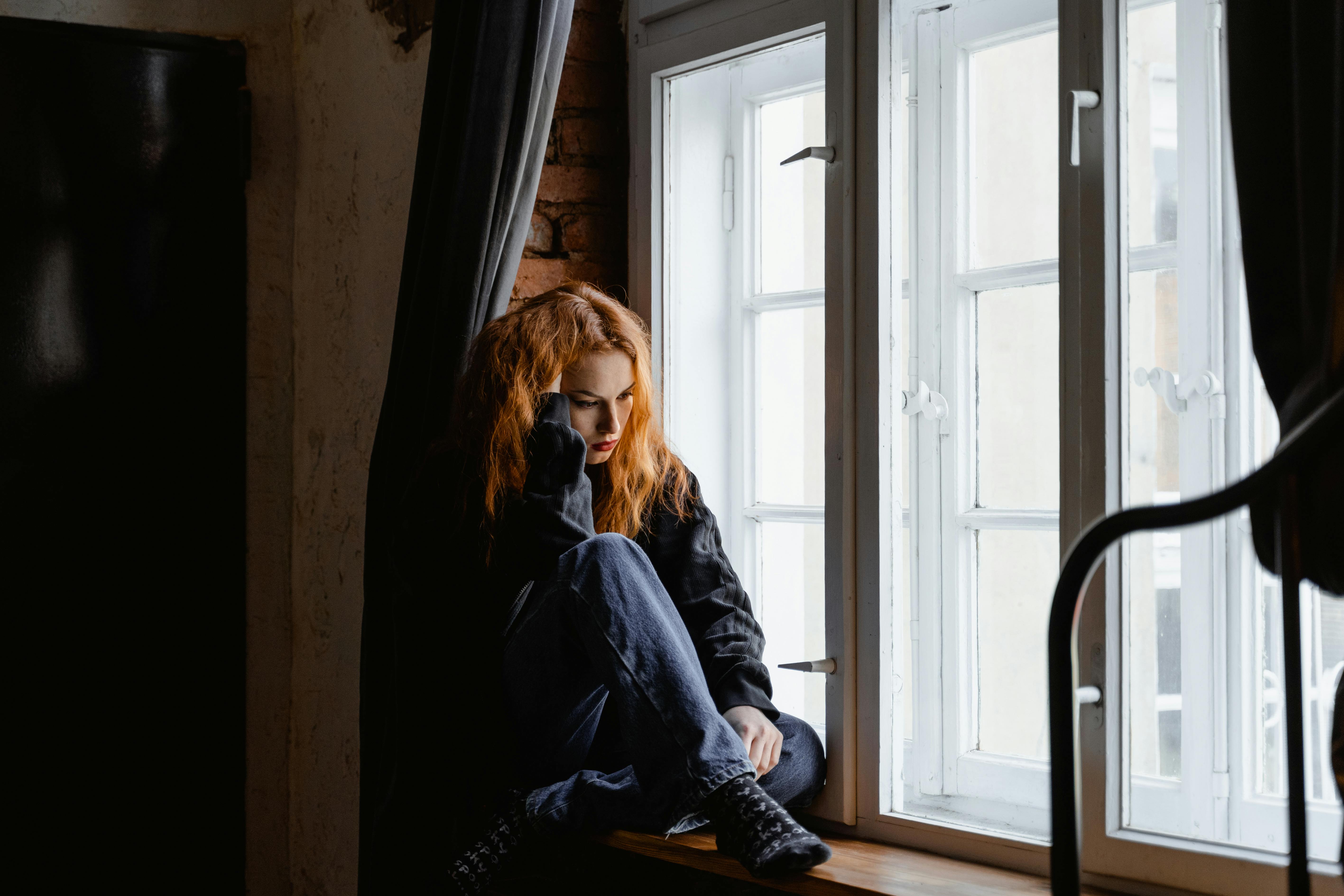 Une femme a l'air contrariée alors qu'elle est assise près d'une fenêtre | Source : Pexels