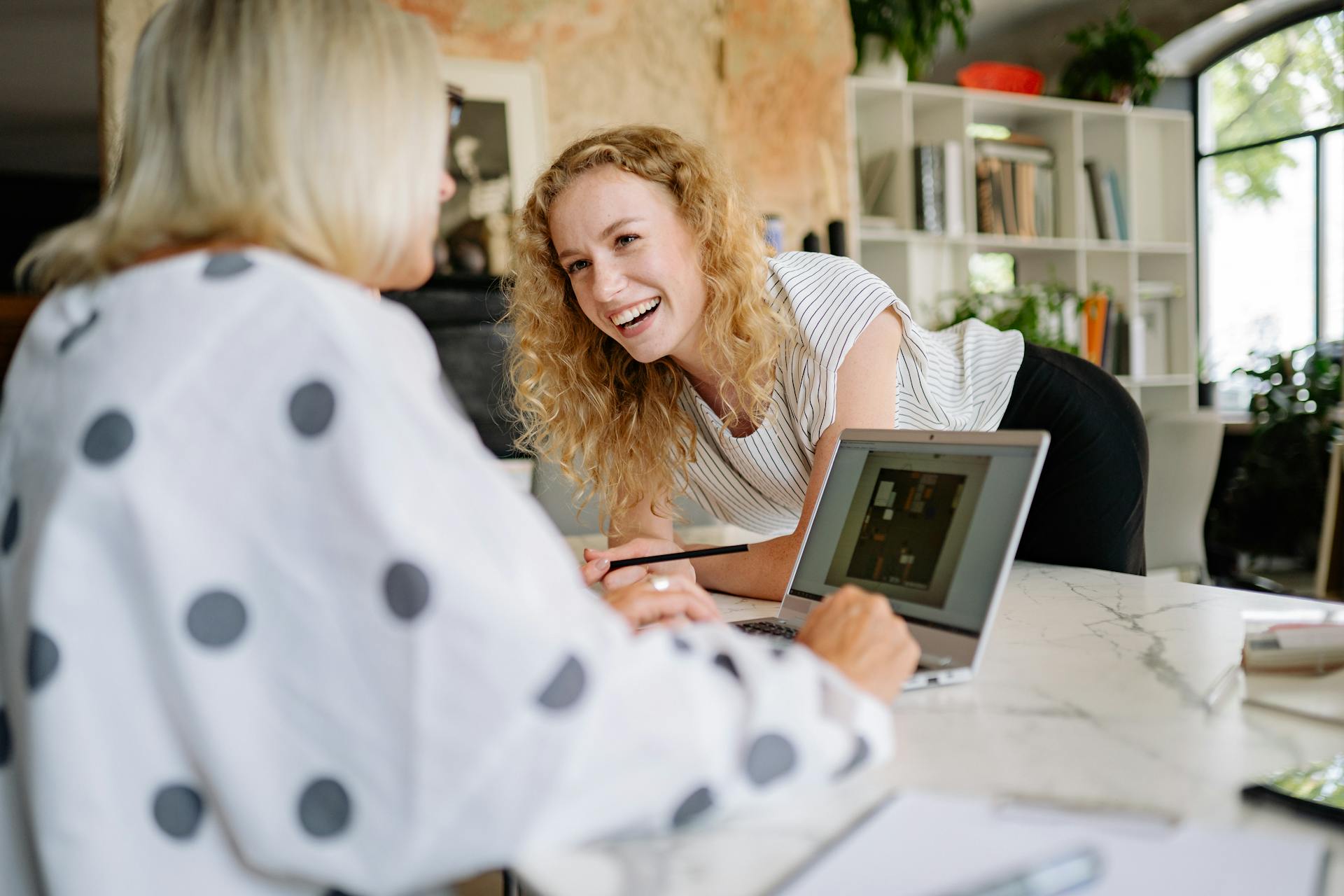 Une femme en train de rire s'appuie sur une table tout en parlant à son collègue de travail | Source : Pexels