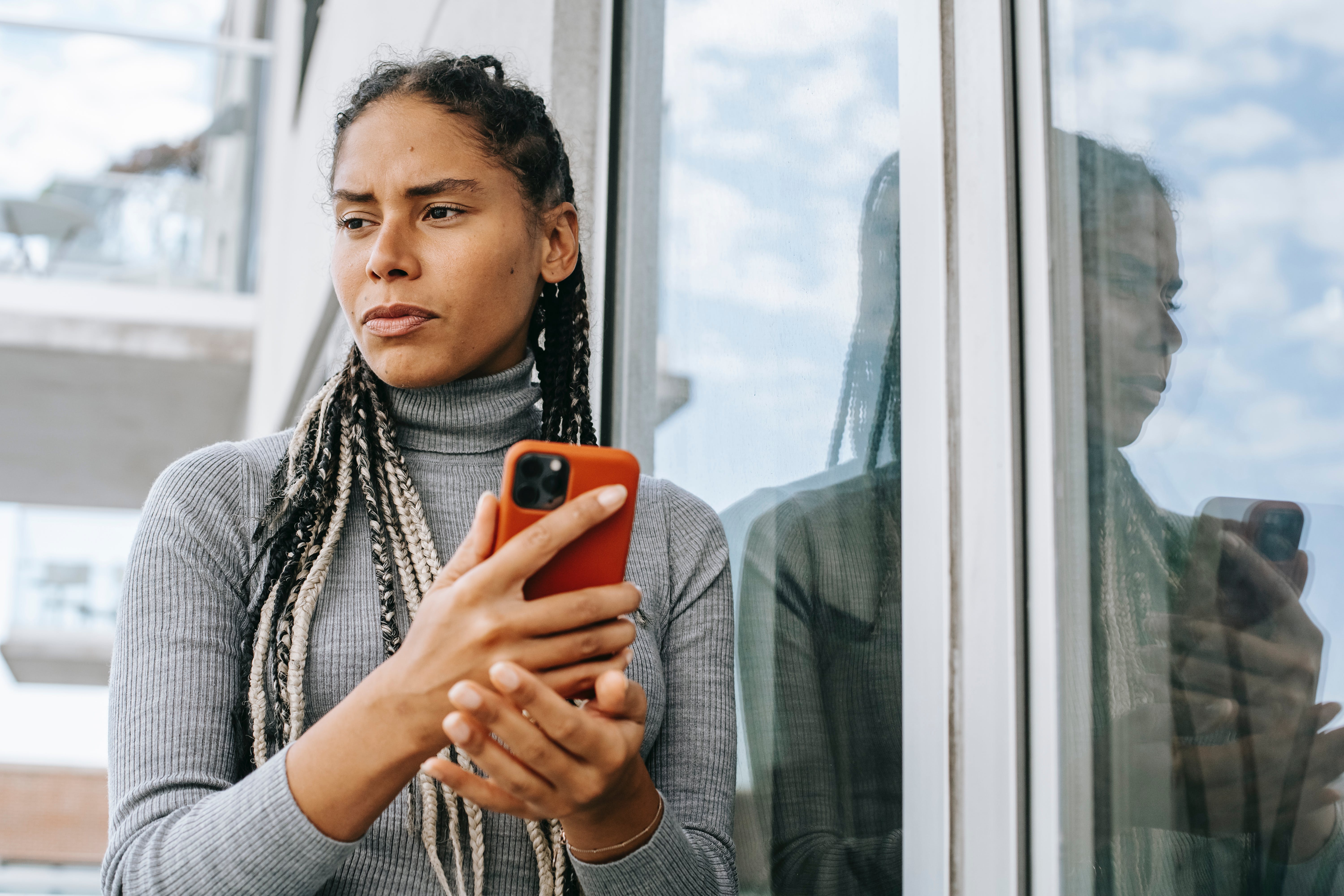 Une femme à l'air contrarié regarde dehors tout en tenant un téléphone | Source : Pexels
