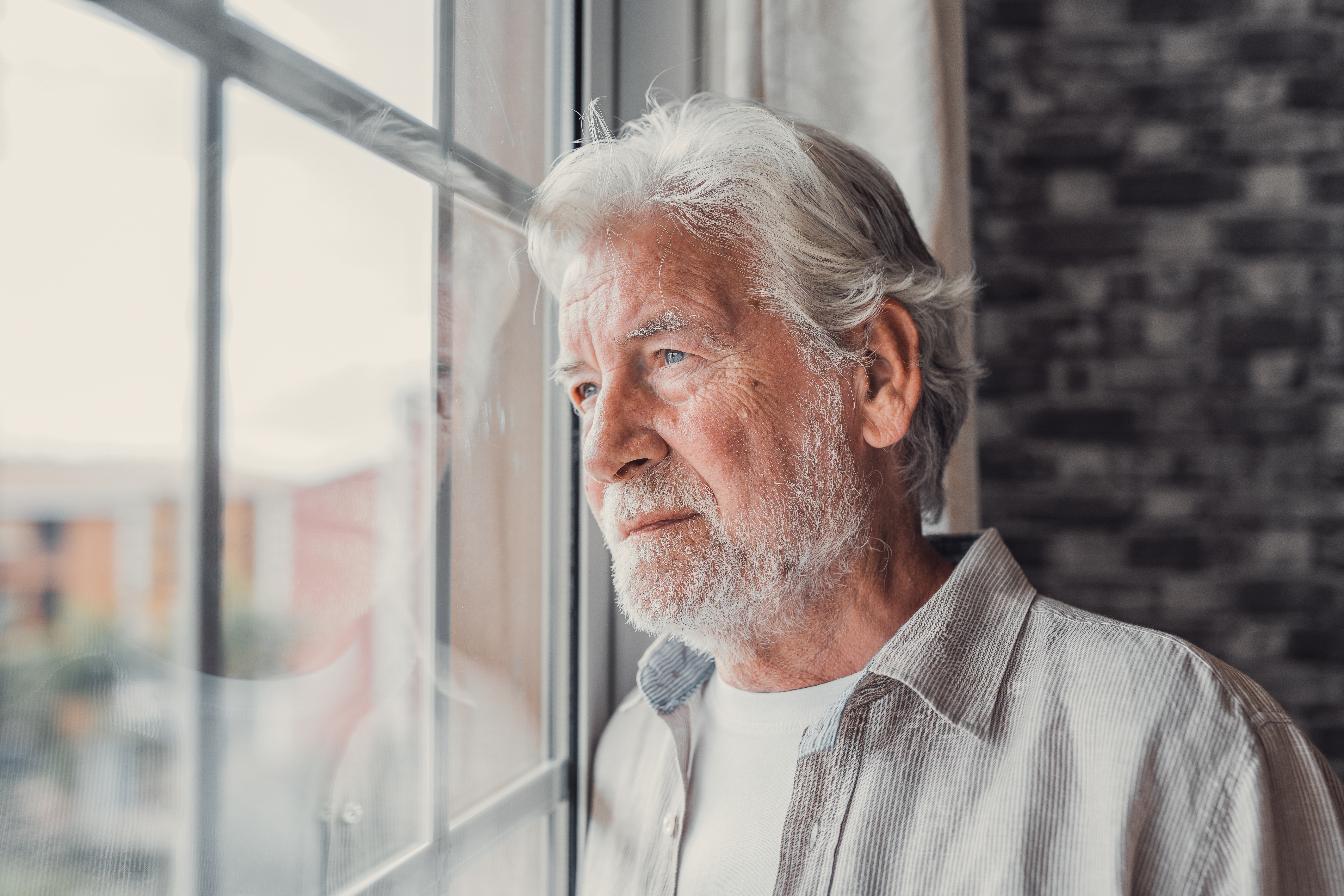 Un homme âgé inquiet se tenant près d'une fenêtre | Source : Shutterstock