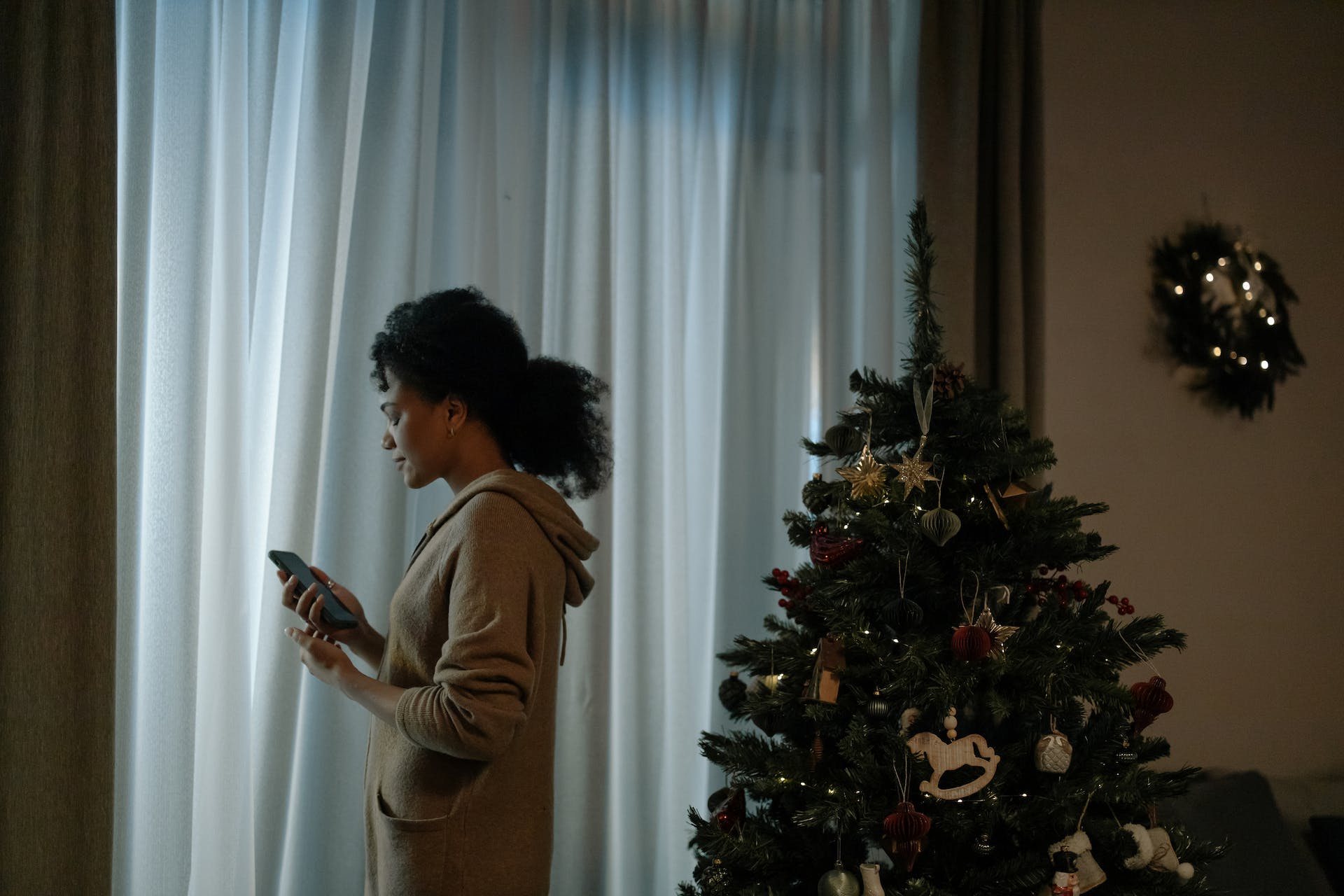 Femme avec un téléphone debout à côté d'un arbre de Noël | Source : Pexels
