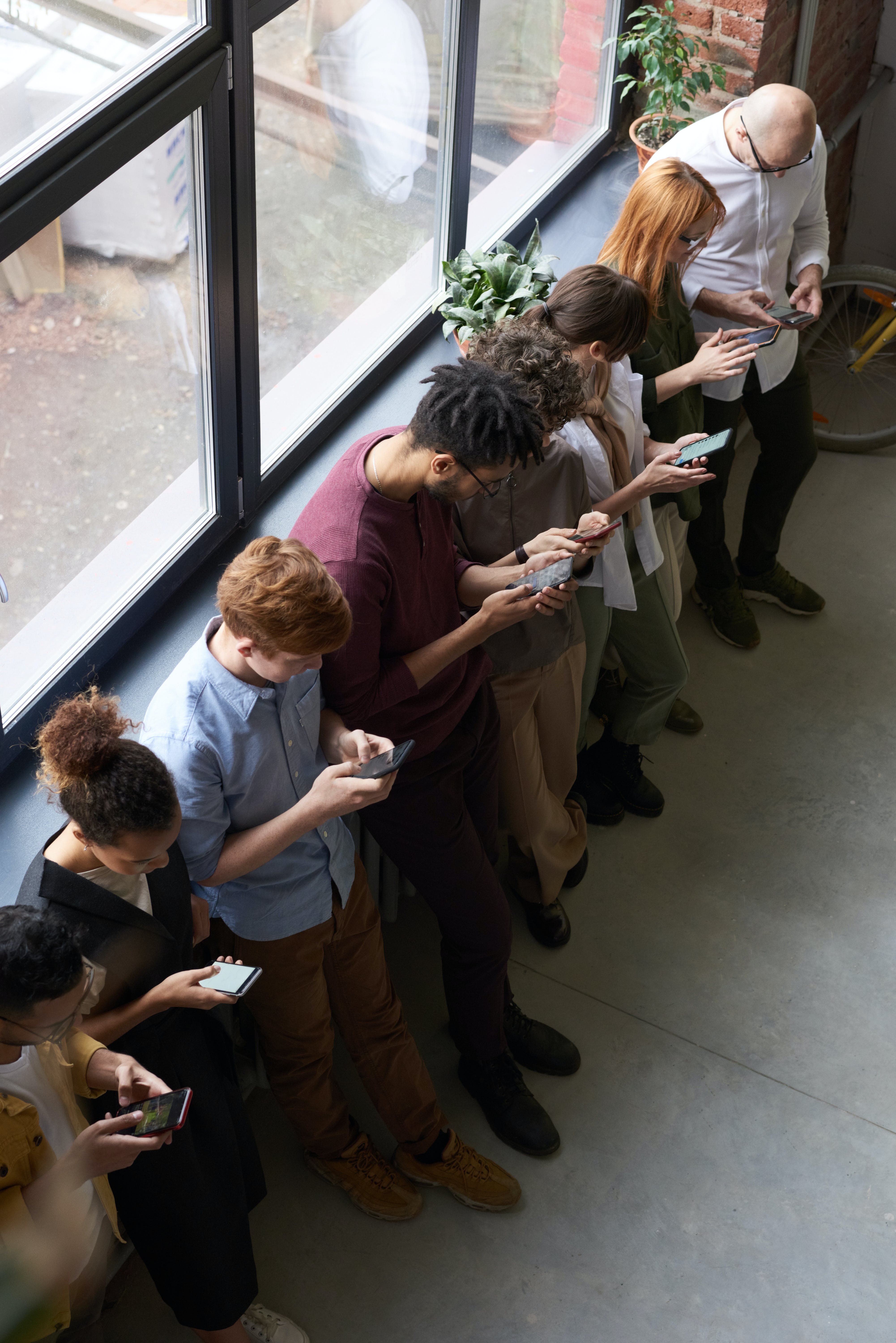 Des personnes font la queue tout en manipulant leur smartphone. | Source : Pexels