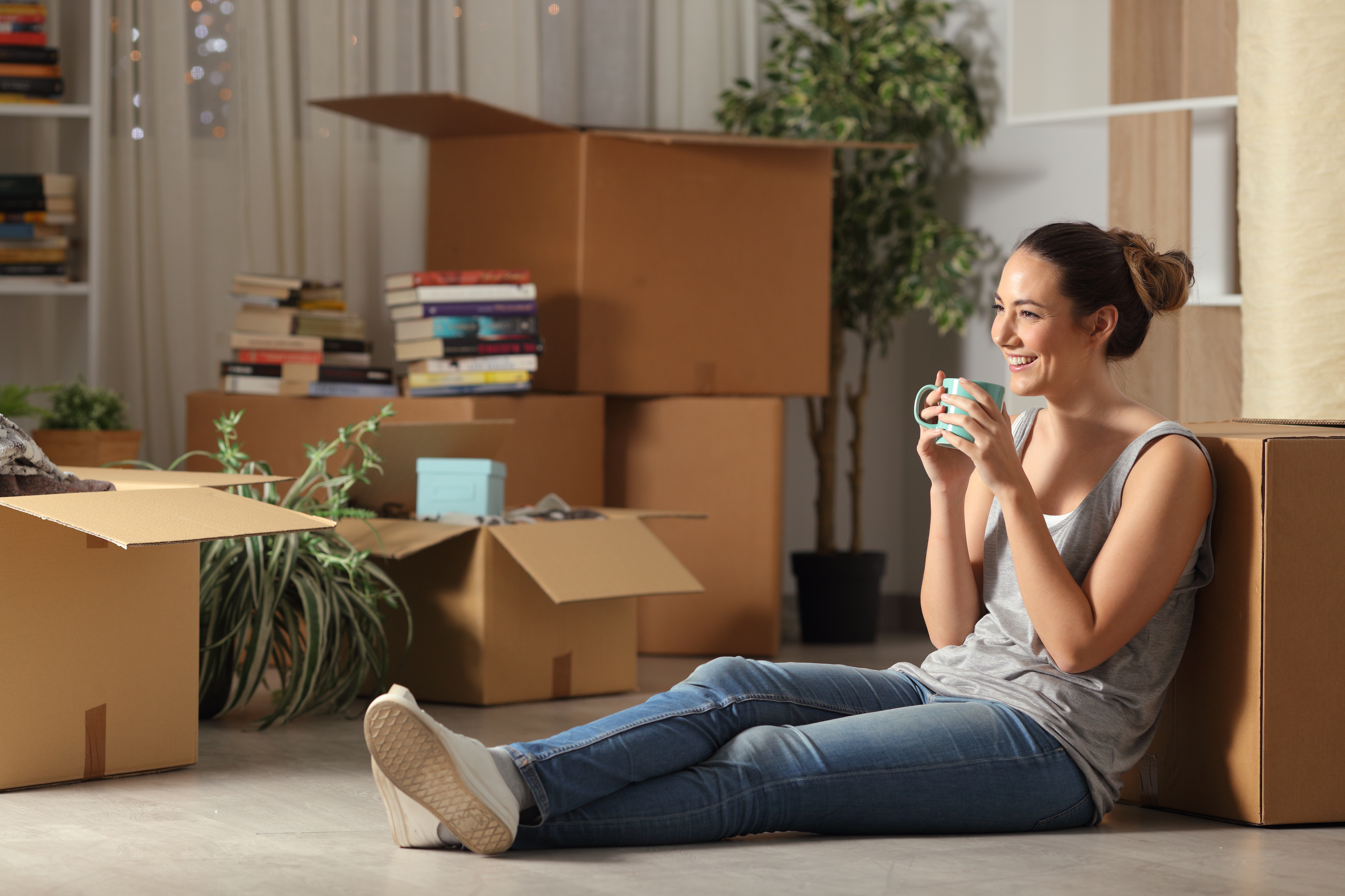 Une jeune fille assise par terre, entourée de cartons, en train de boire un café | Source : Shutterstock
