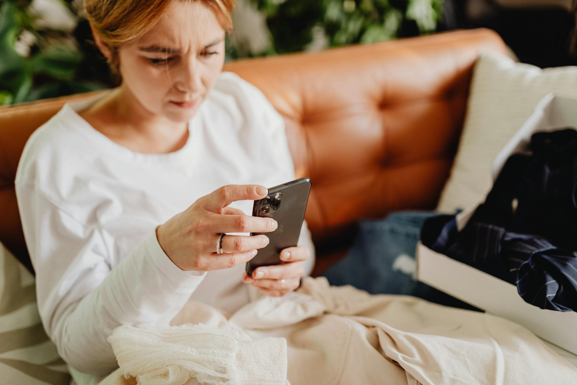 Une femme assise sur le canapé et tenant son smartphone | Source : Pexels