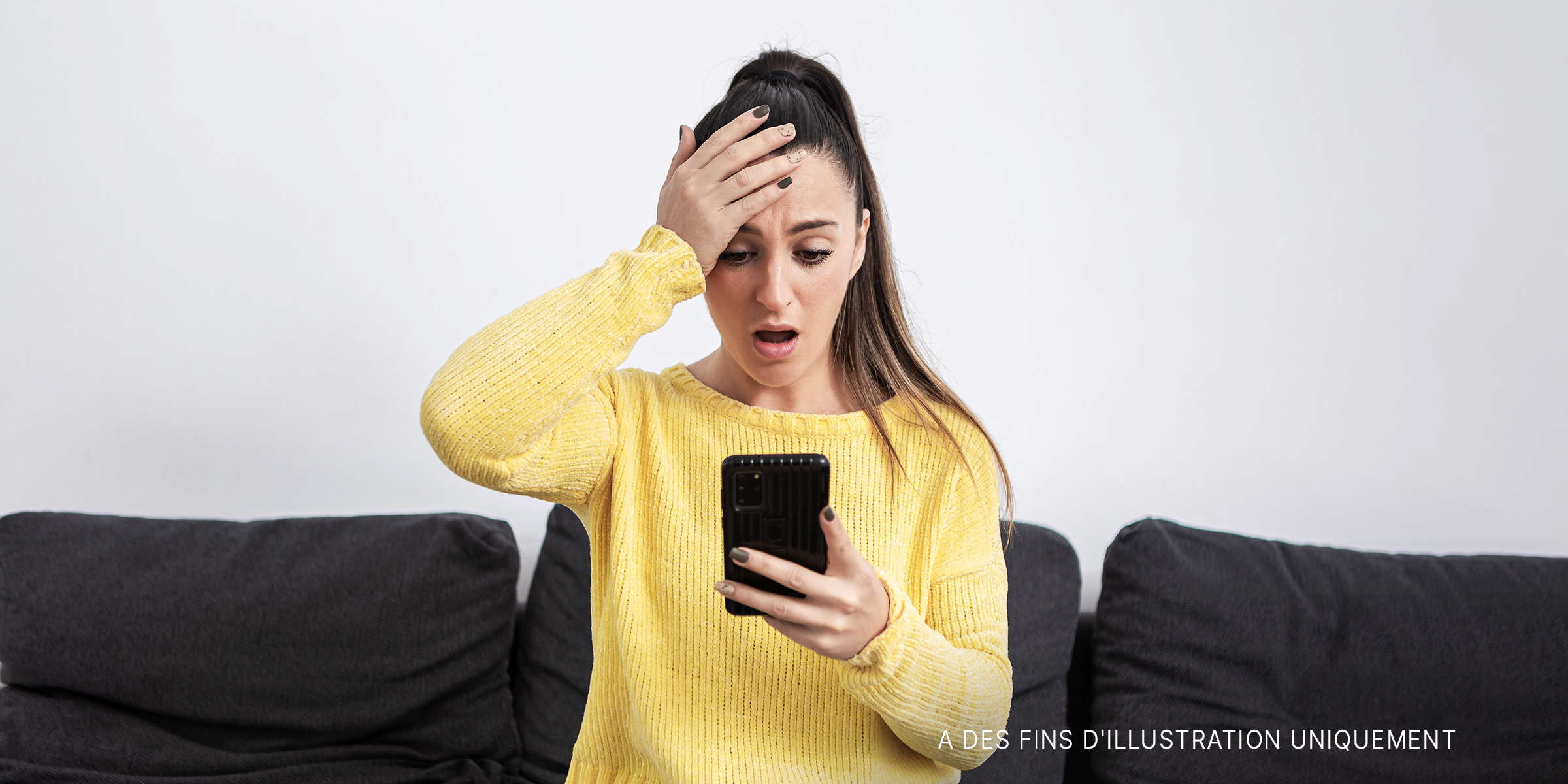 Une femme est choquée alors qu'elle regarde l'écran de son téléphone portable | Source : Getty Images