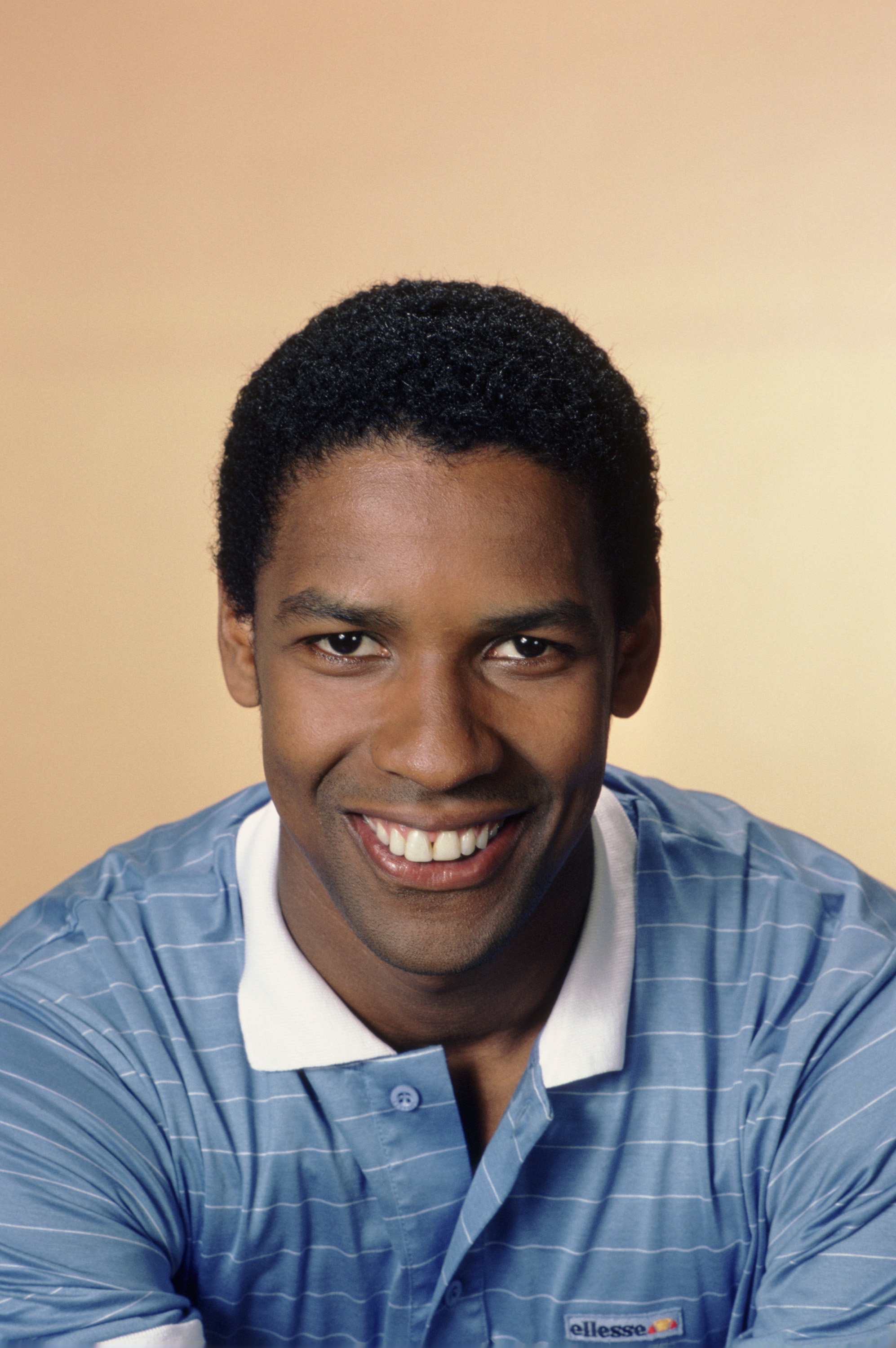 Denzel Washington pose dans un polo bleu pâle au début de sa carrière. Avec sa petite coupe afro et son visage rasé de près, ce portrait capture tout le charme de la star montante pendant le tournage de « St. Elsewhere ».