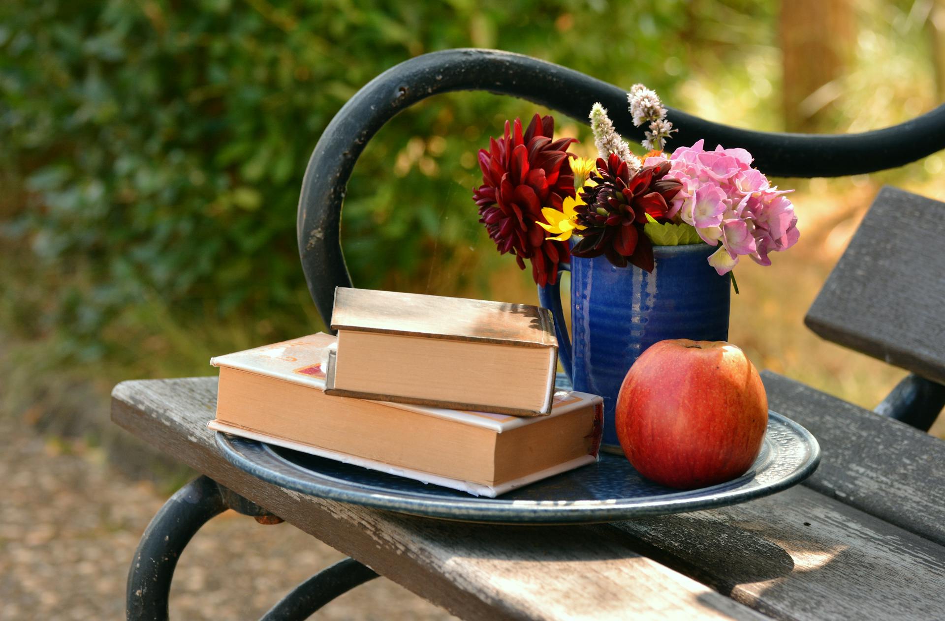 Deux livres placés l'un sur l'autre à côté d'un vase à fleurs et d'une pomme rouge | Source : Pexels