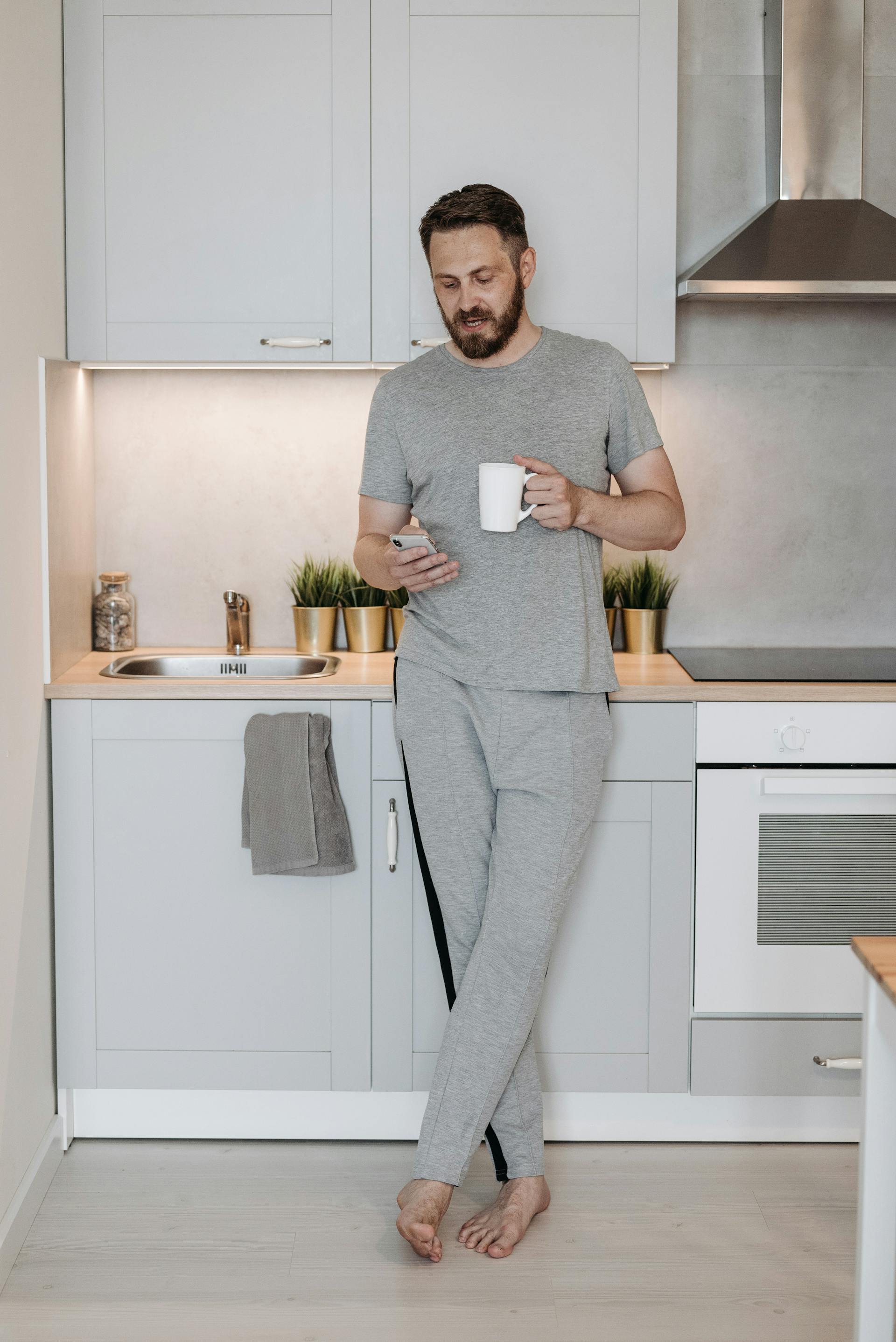 Un homme qui fait défiler son téléphone dans une cuisine | Source : Pexels