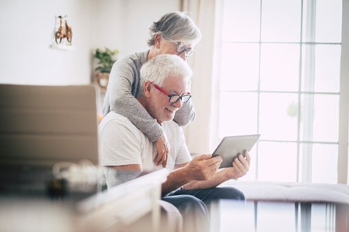 Un couple de personnes âgées souriant et regardant la  tablette à la maison. | Photo : Getty Images