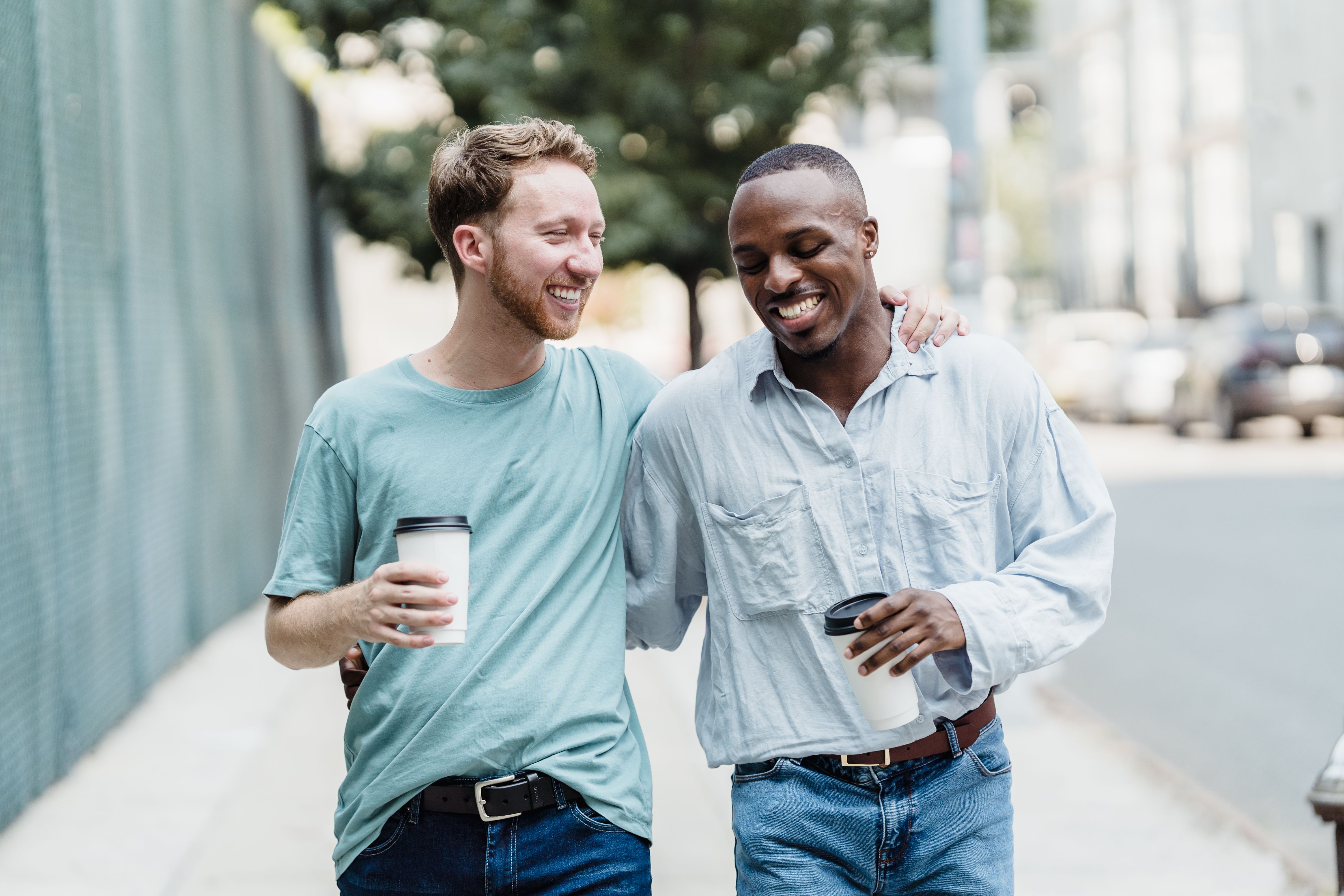 Deux amis qui se promènent en rigolant dans une rue de la ville, en train de prendre un café ensemble en terrasse | Source : Pexels