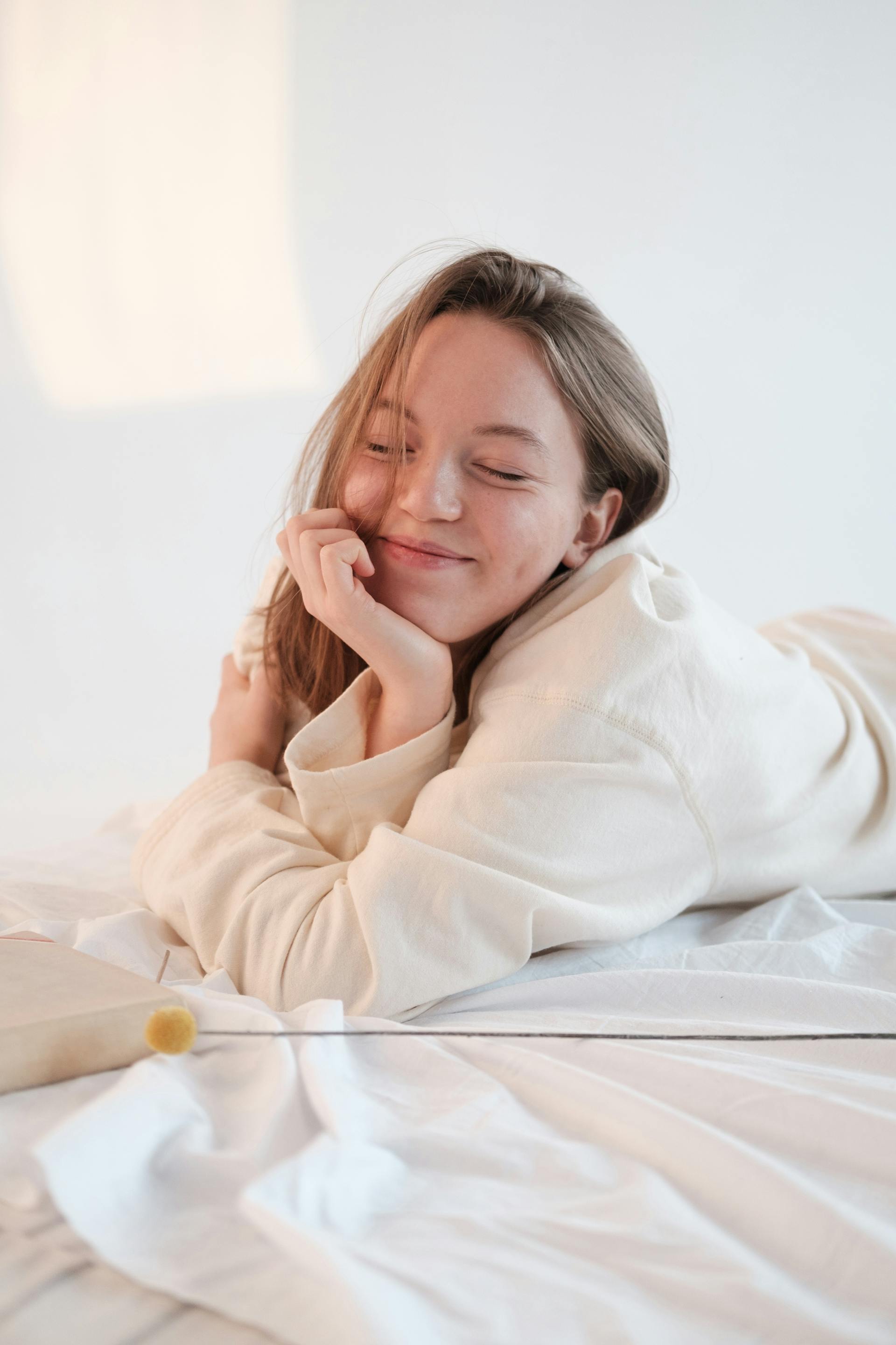 Une femme souriante se reposant dans son lit les yeux fermés | Source : Pexels