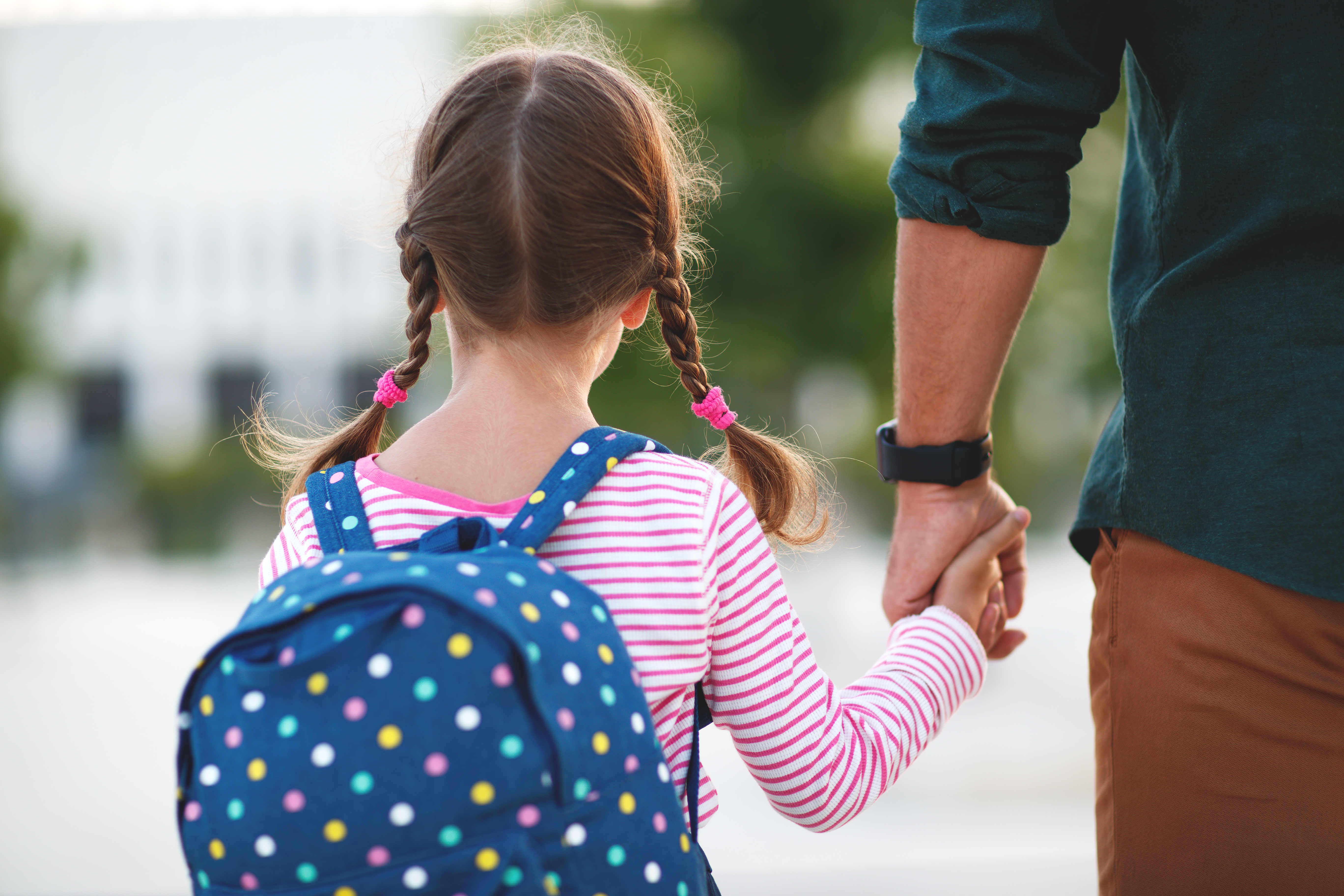 Une petite fille tient la main de son père en allant à l'école | Source : Shutterstock