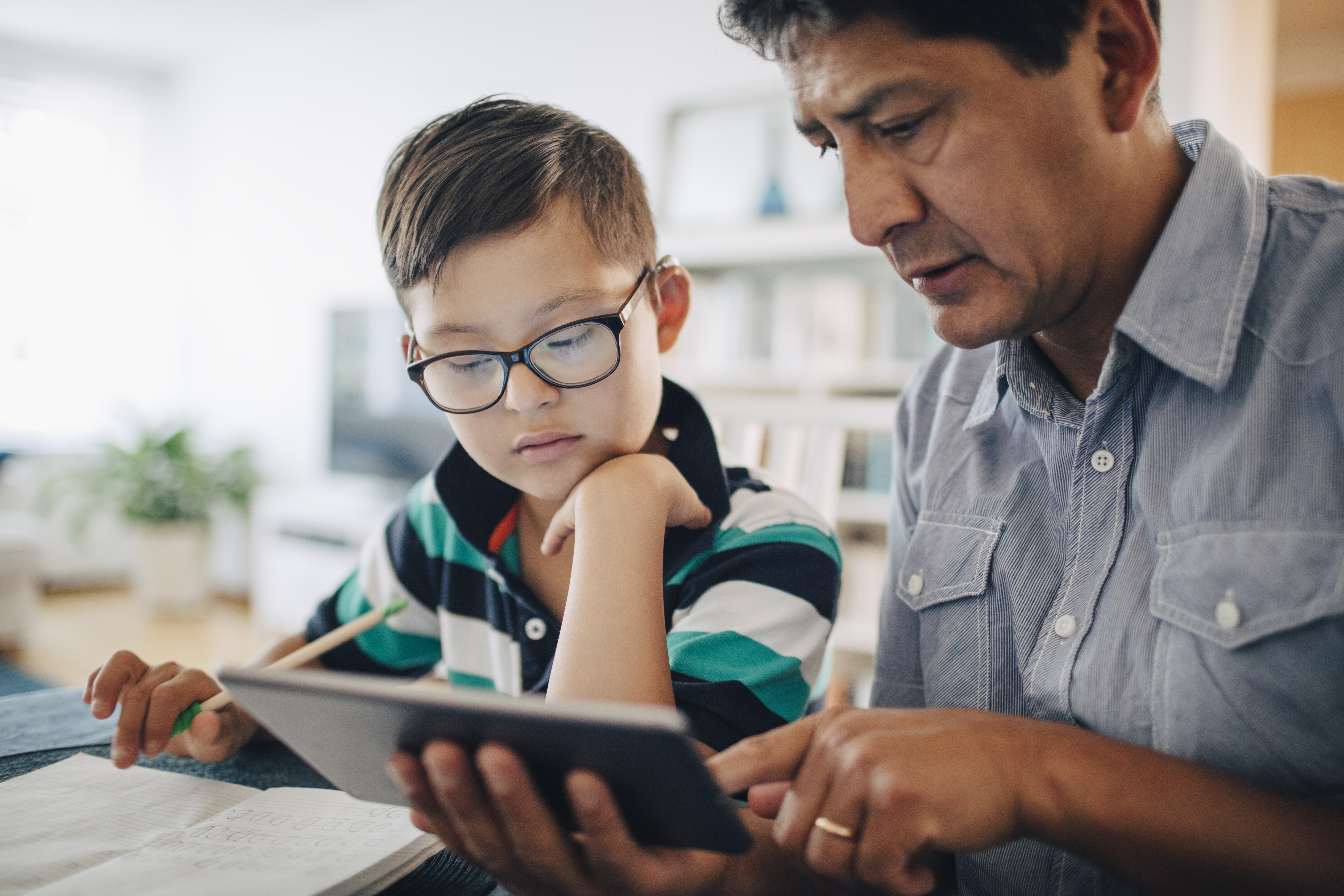 Un père montre une tablette numérique à son fils alors qu'il étudie à table | Source : Getty Images