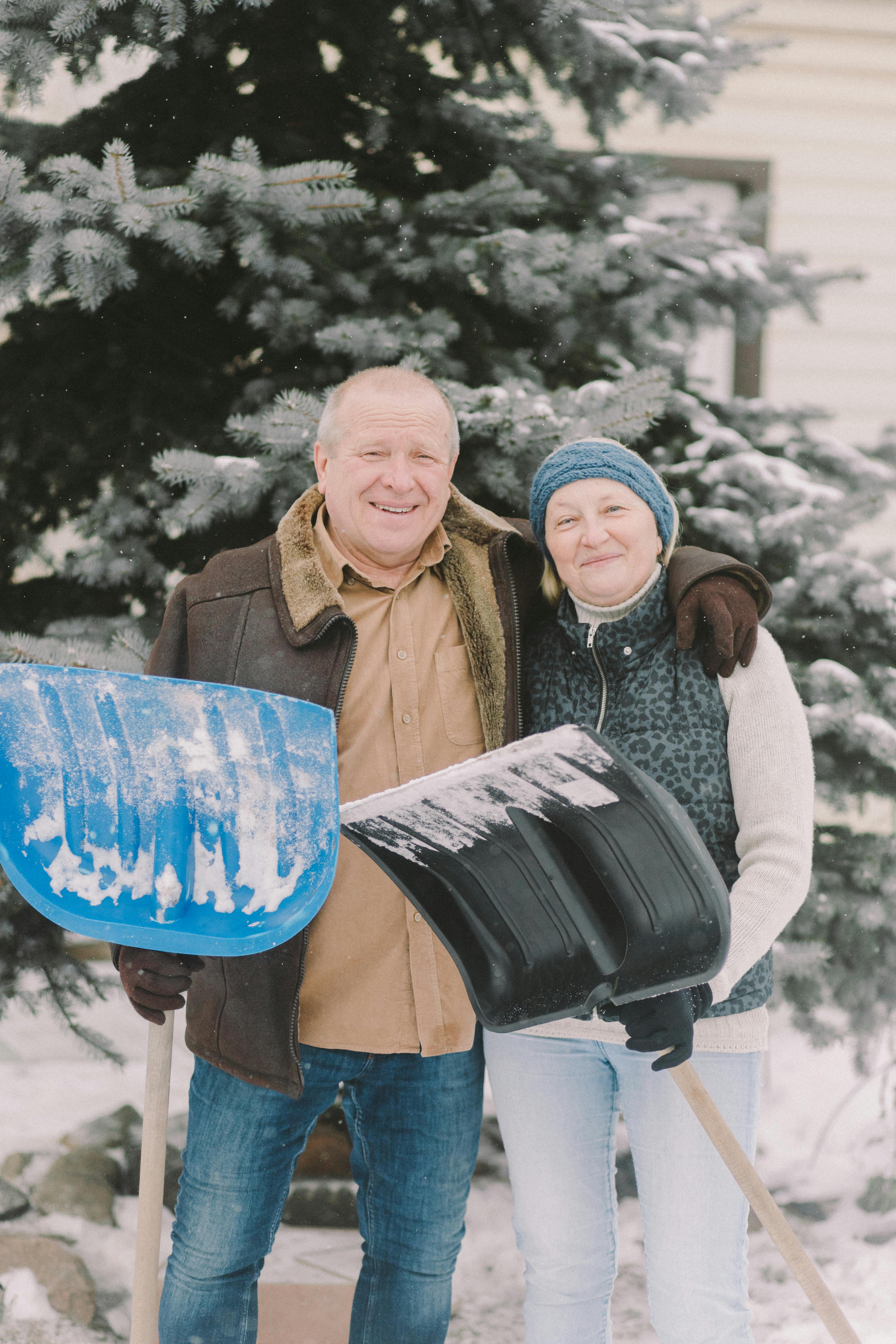 Un couple heureux d'âge moyen s'embrasse en tenant des pelles à neige | Source : Pexels