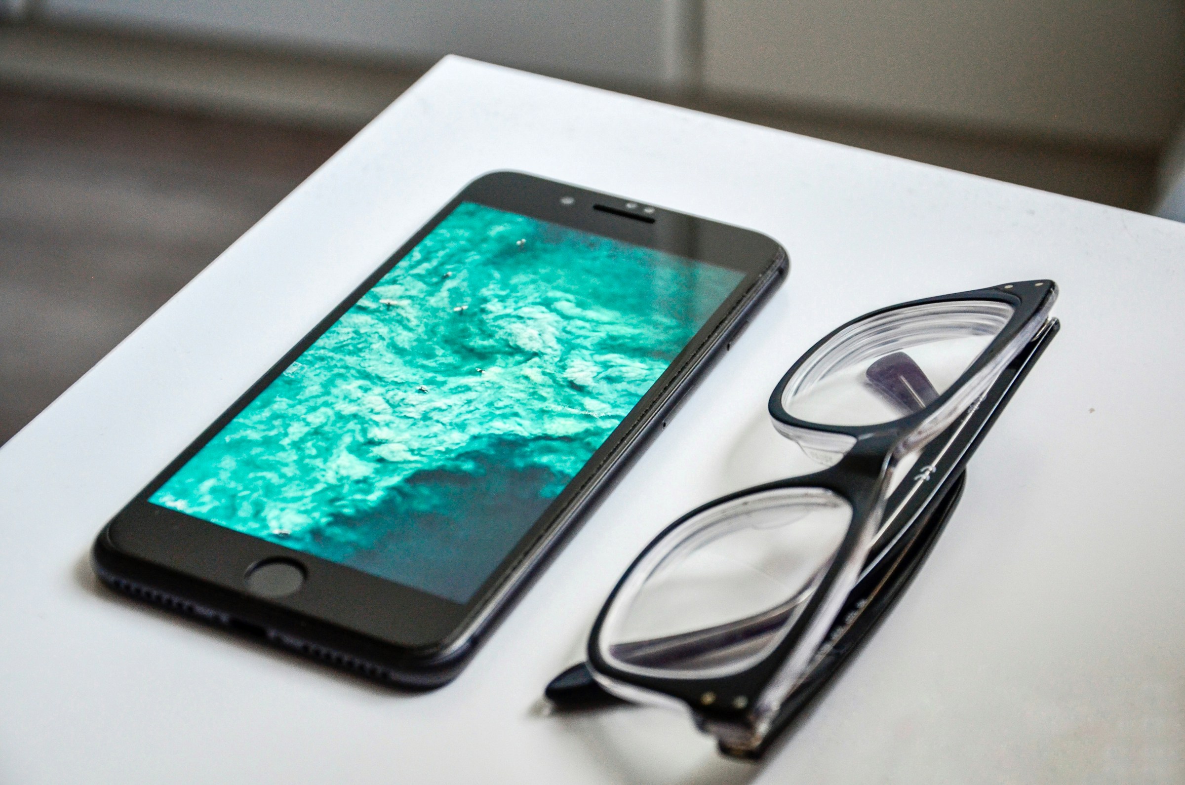 Un smartphone et une paire de lunettes posés sur une table | Source : Unsplash