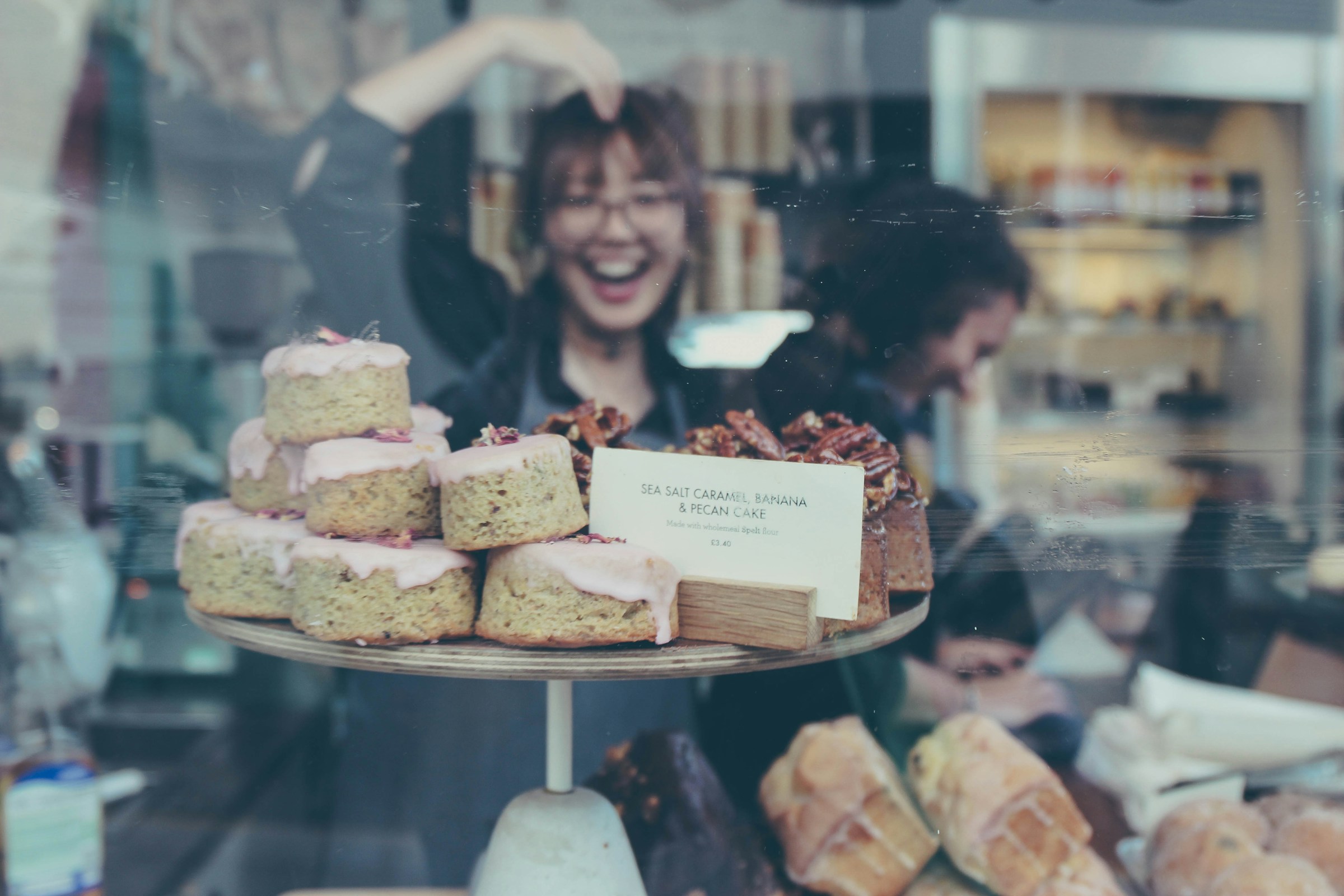 Le reflet d'une jeune femme souriante dans la vitre d'un présentoir de boulangerie | Source : Unsplash