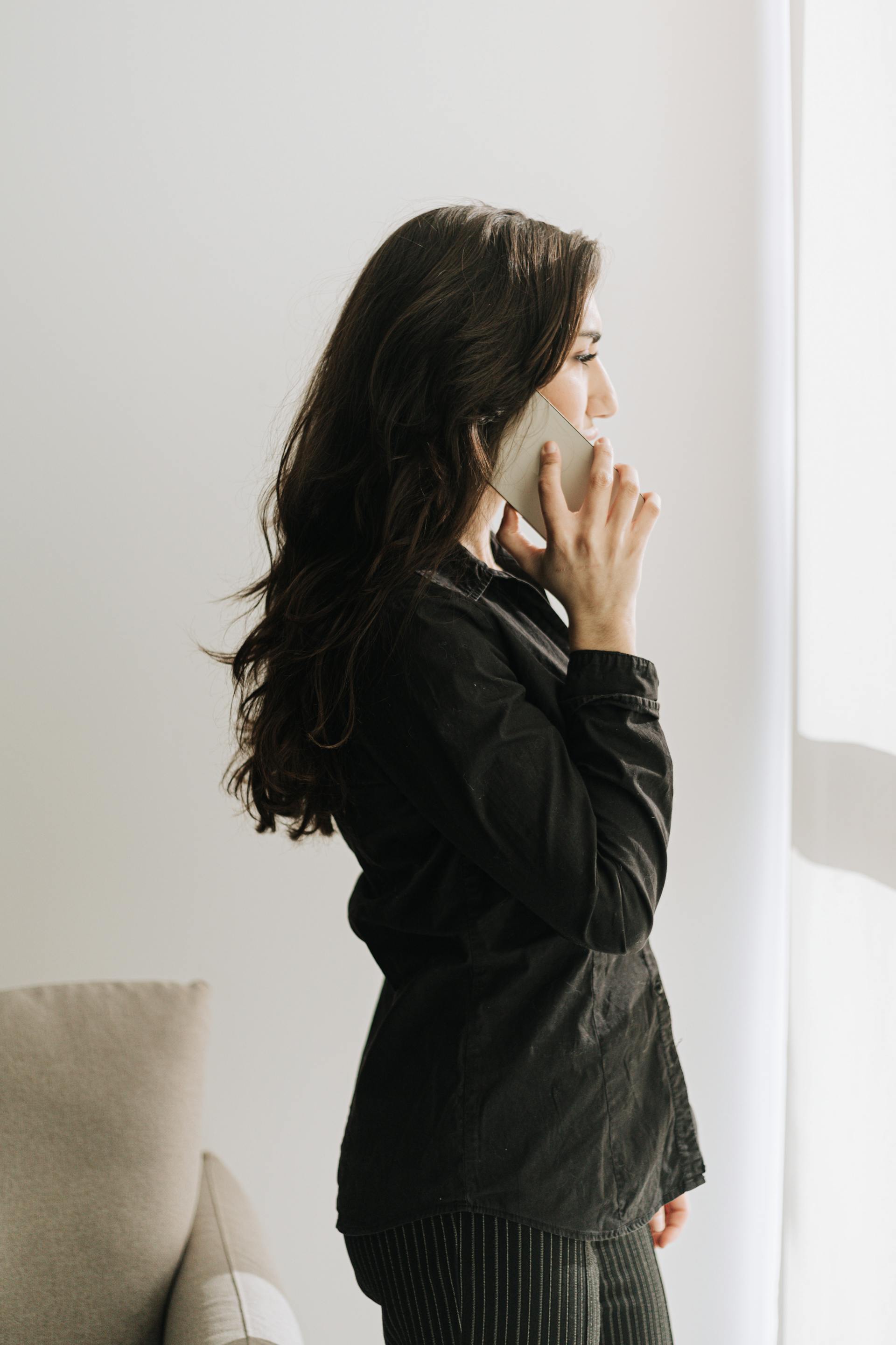 Une femme en train de téléphoner, debout près d'une fenêtre | Source : Pexels