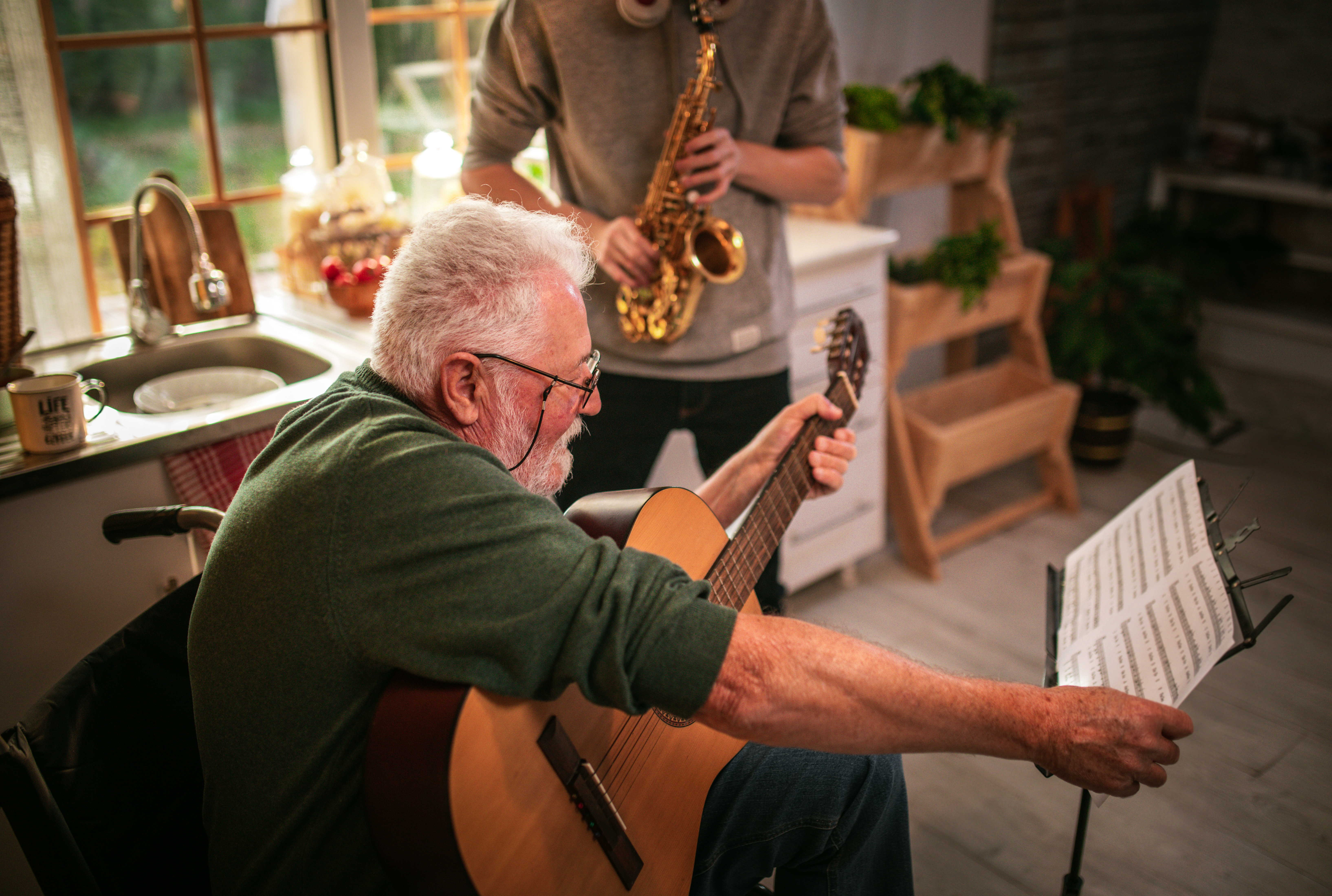 Un homme âgé heureux et son petit-fils s'amusent en jouant du saxophone et de la guitare à la maison. | Source : Getty Images