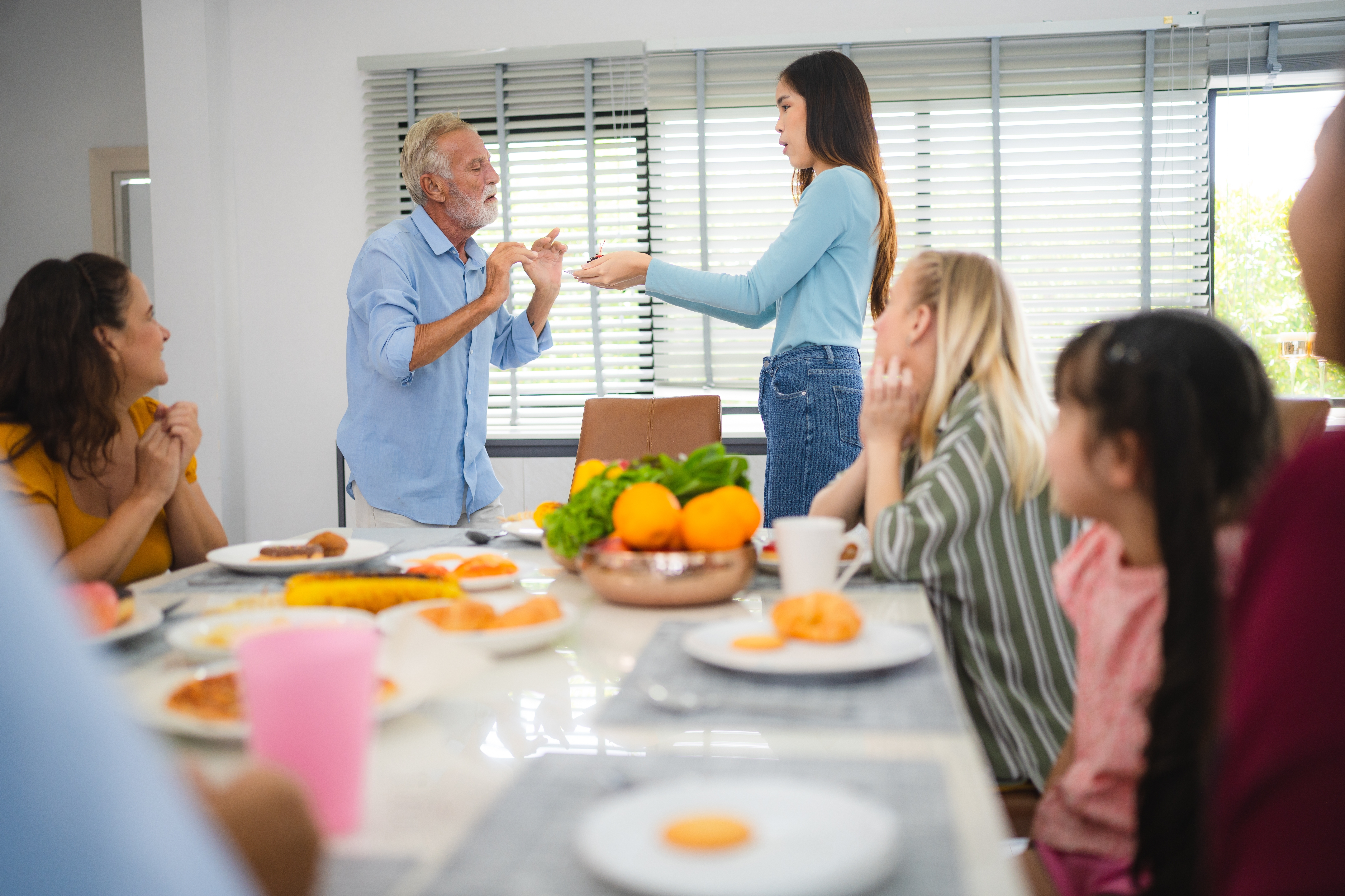 Un homme âgé parlant à une jeune fille pendant le dîner familial dans la salle à manger | Source : Shutterstock