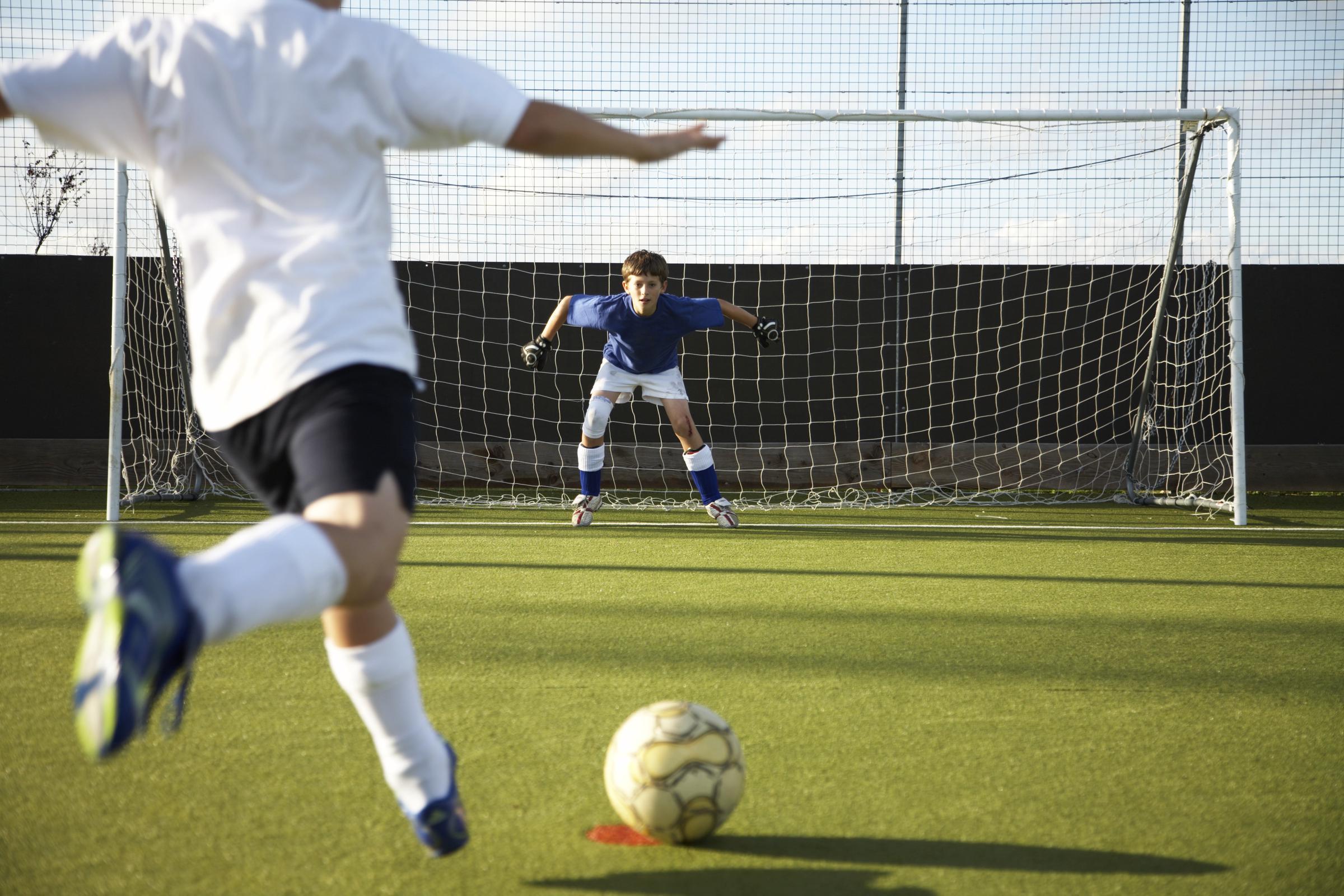 Un garçon (9-11 ans) tirant au but avec un ballon de football, vue de derrière I Source : Getty Images