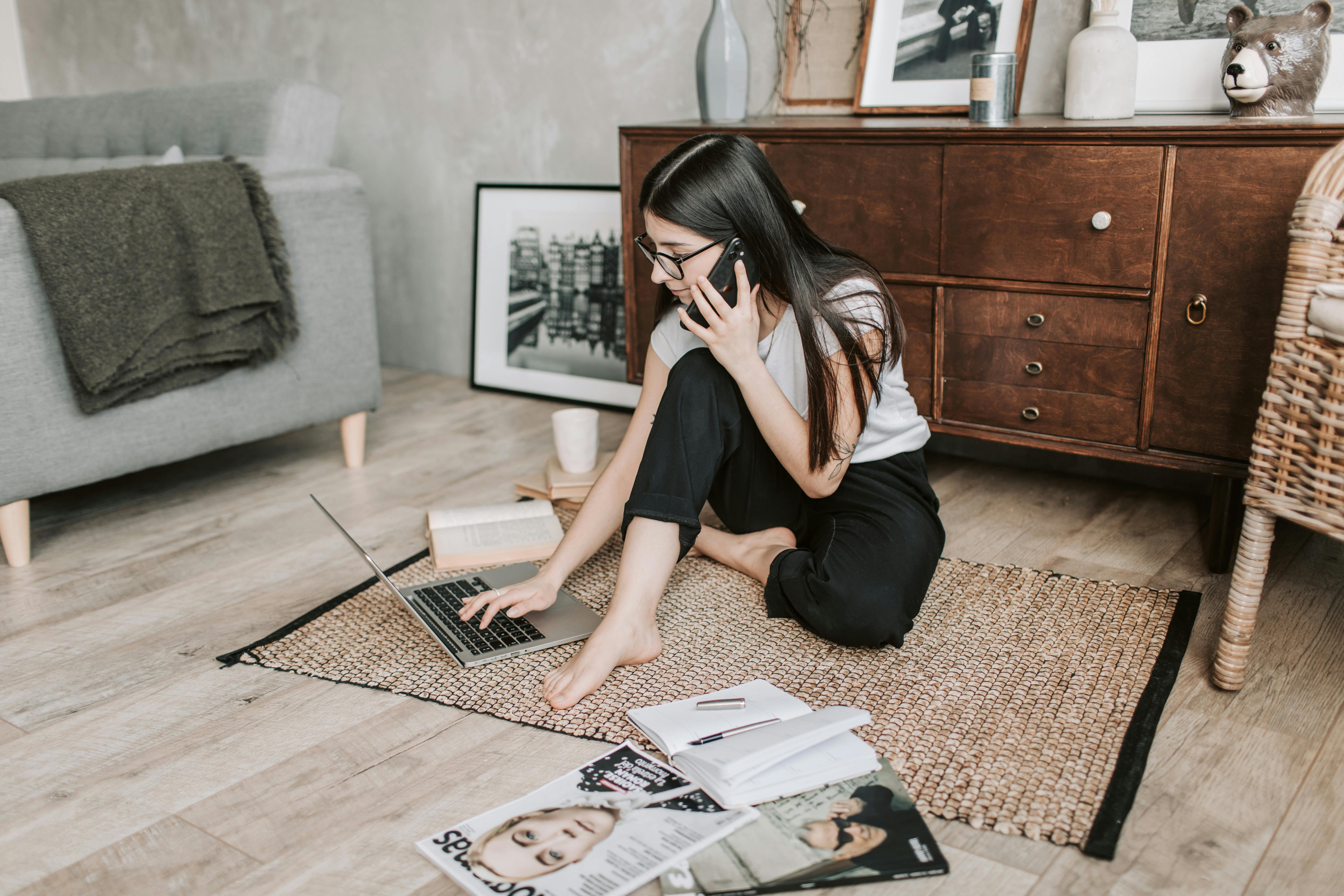 Une jeune fille au téléphone avec un ordinateur portable, des livres et des magazines autour d'elle | Source : Pexels