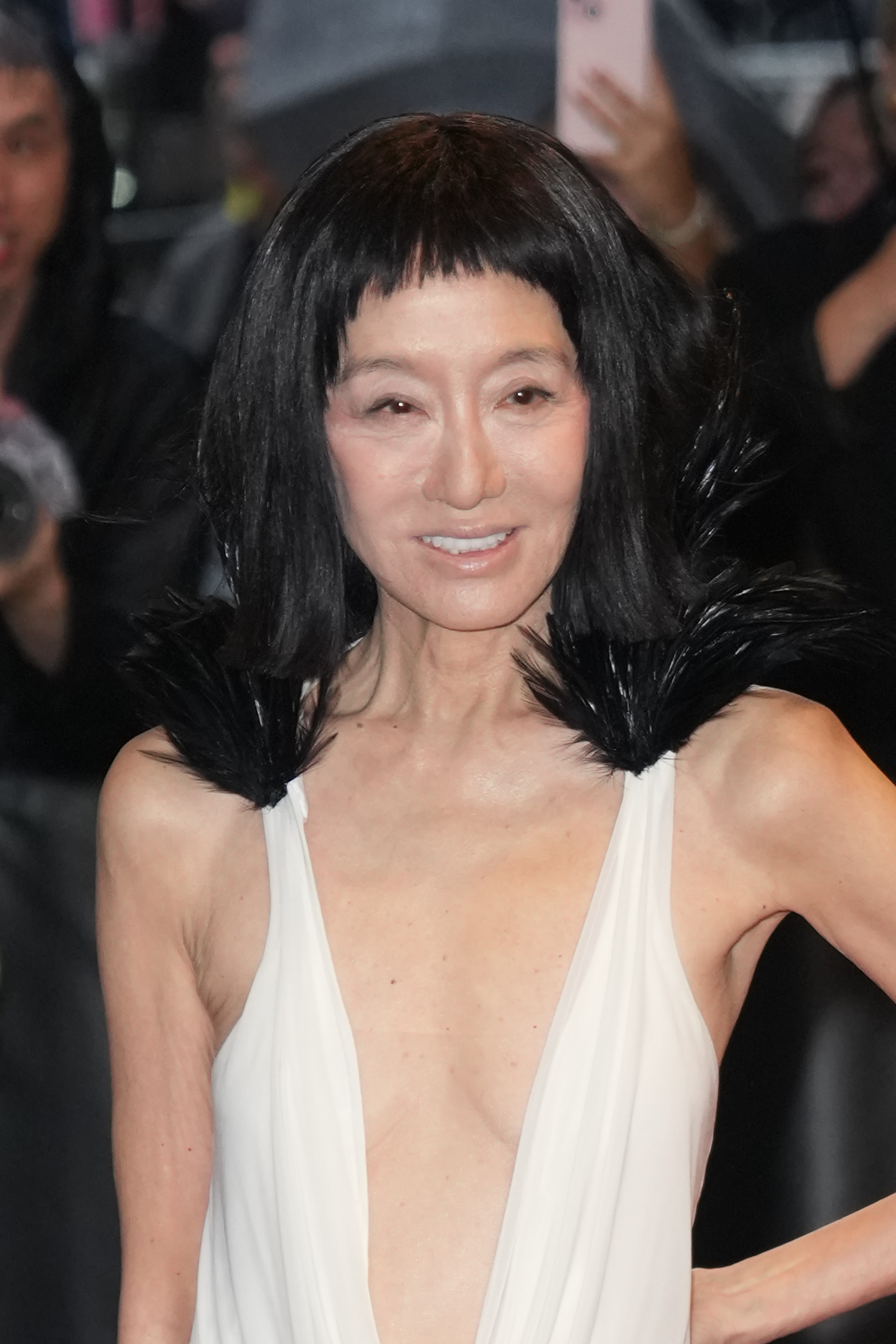 Vera Wang sourit aux caméras dans une robe ivoire plongeante avec des accents de plumes dramatiques, révélant un côté plus doux à son ensemble audacieux du tapis rouge.