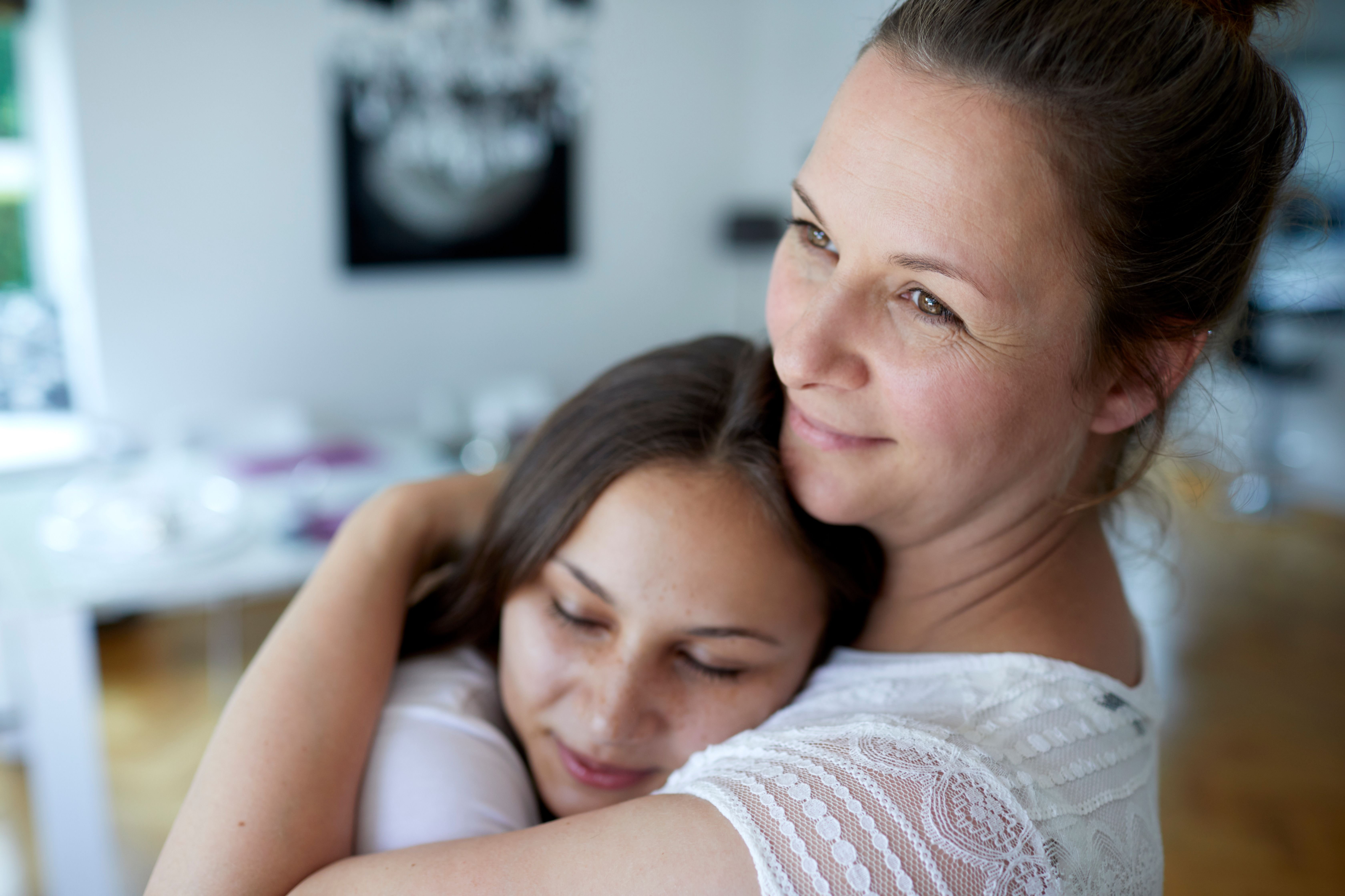 Une mère et sa fille adolescente s'embrassant à la maison. | Source : Getty Images