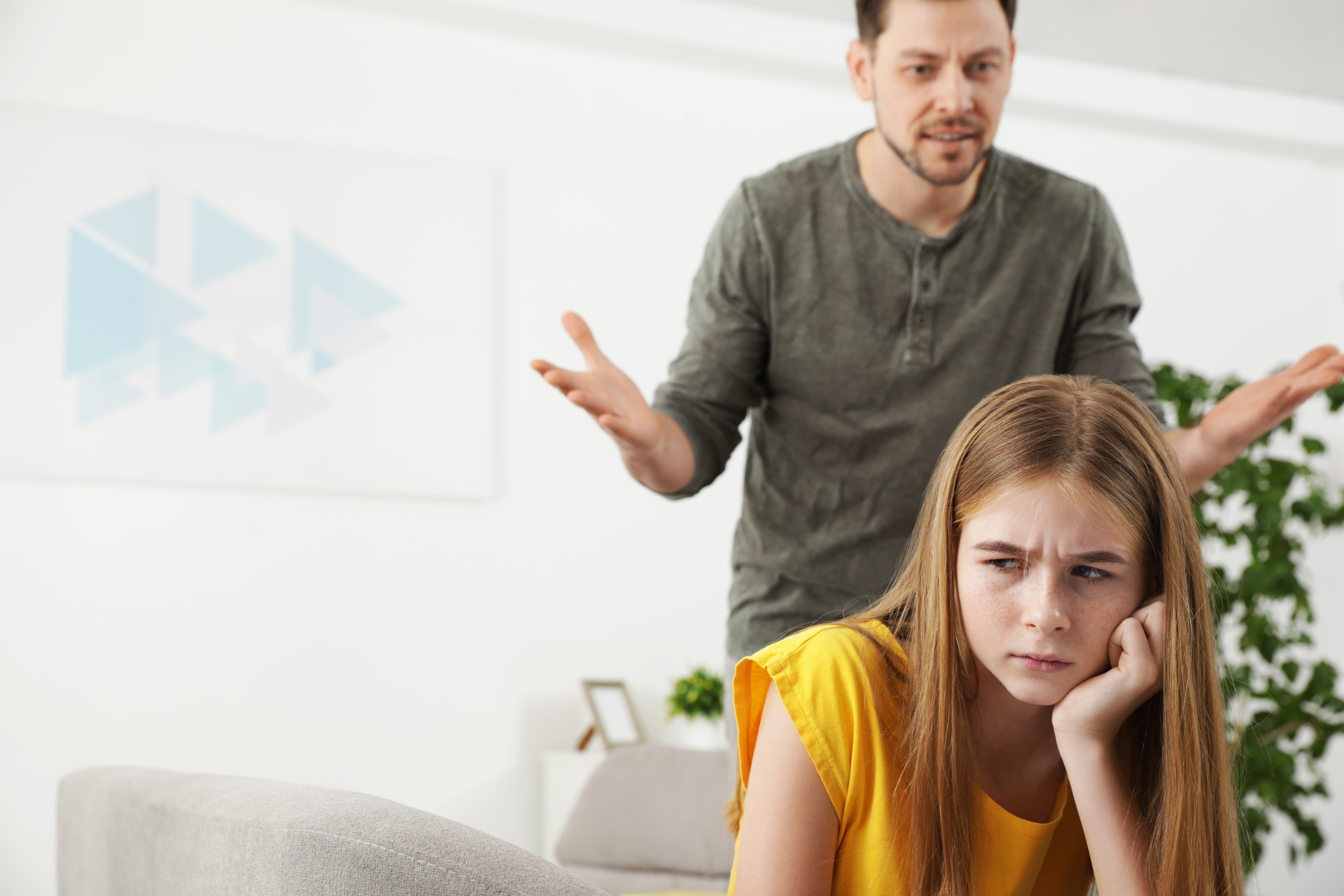 Un homme en colère se tenant derrière une fille assise sur un canapé | Source : Shutterstock