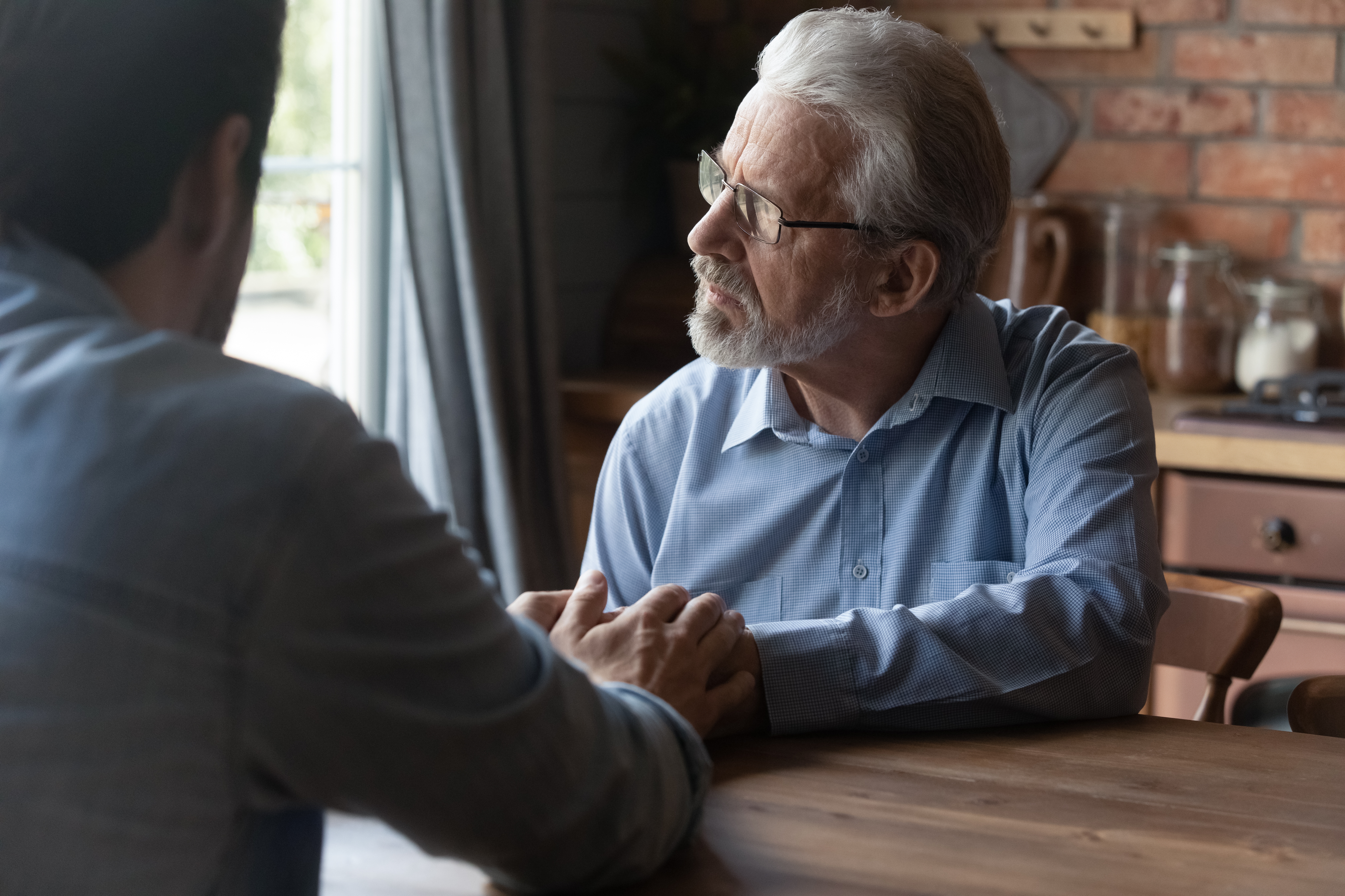 Un jeune homme réconforte un homme plus âgé qui regarde ailleurs | Source : Shutterstock