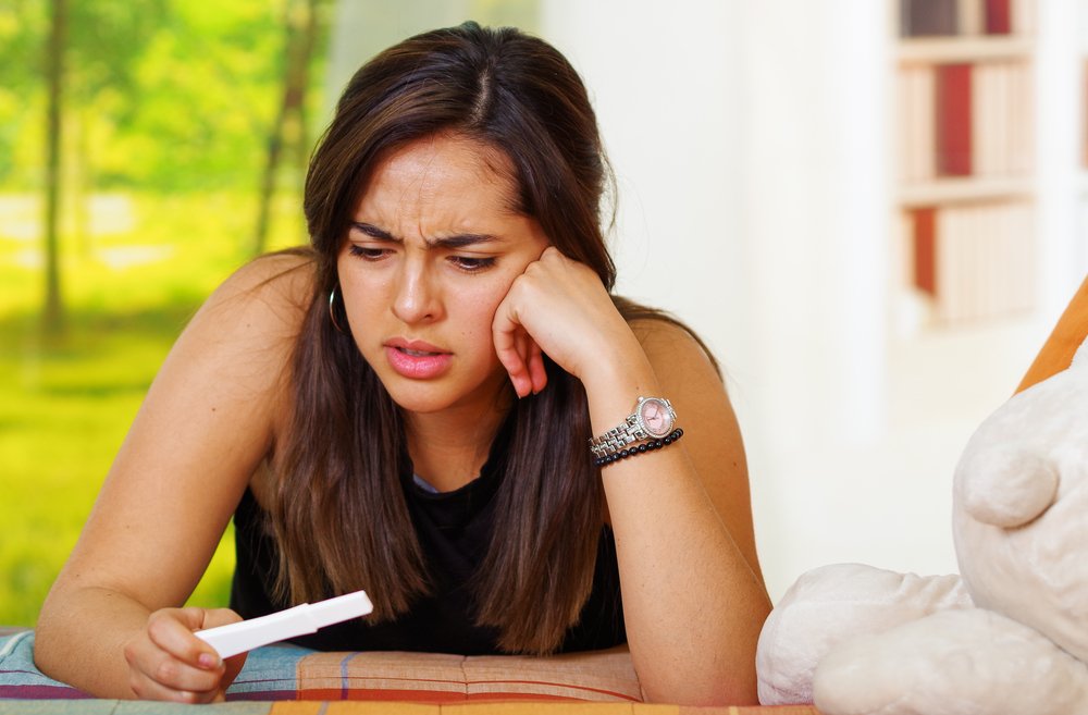 Une jolie jeune femme brune regardant avec incrédulité le résultat de son test de grossesse. | Shutterstock