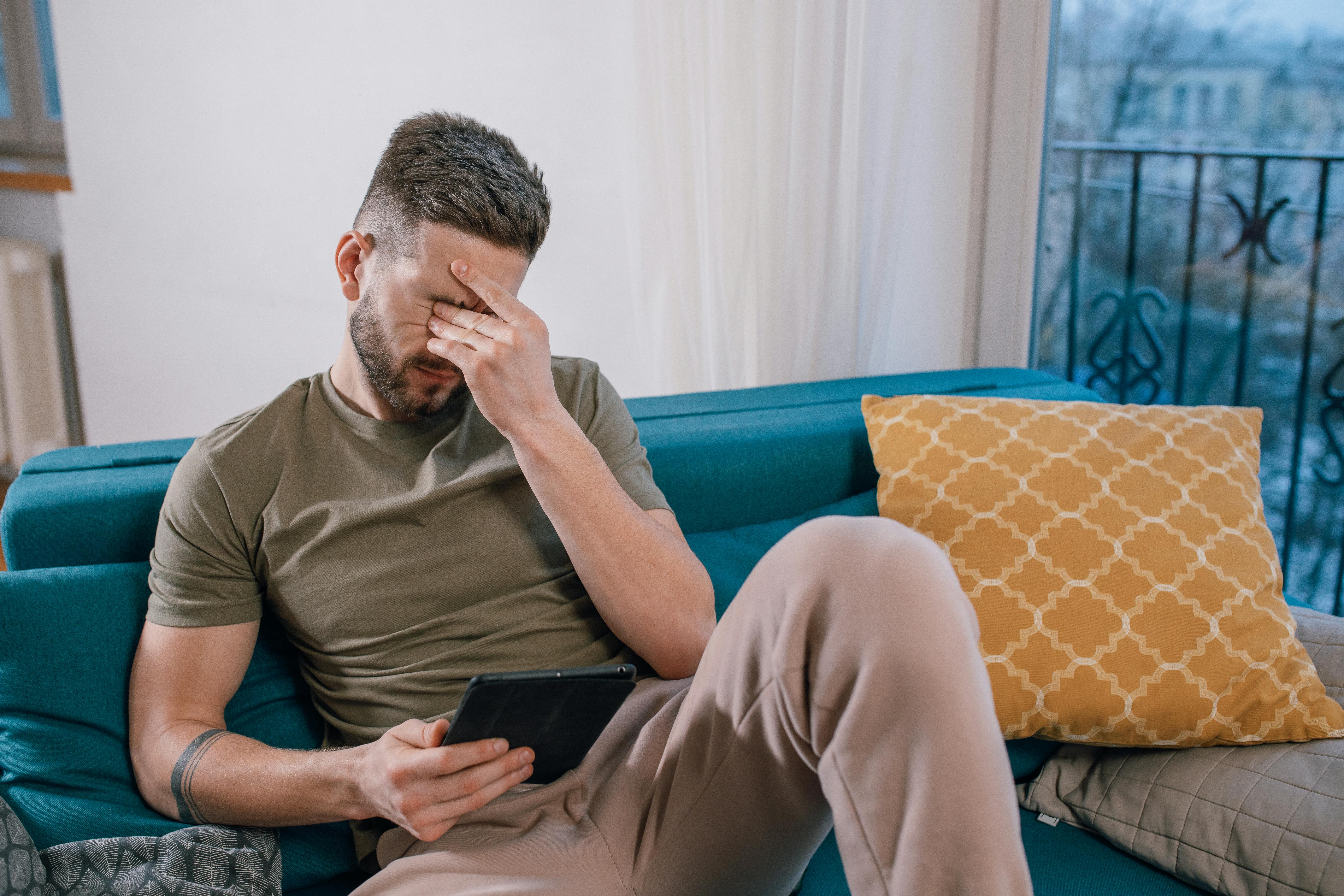 Un homme qui pleure tout en étant assis et en regardant quelque chose sur une tablette | Source : Pexels