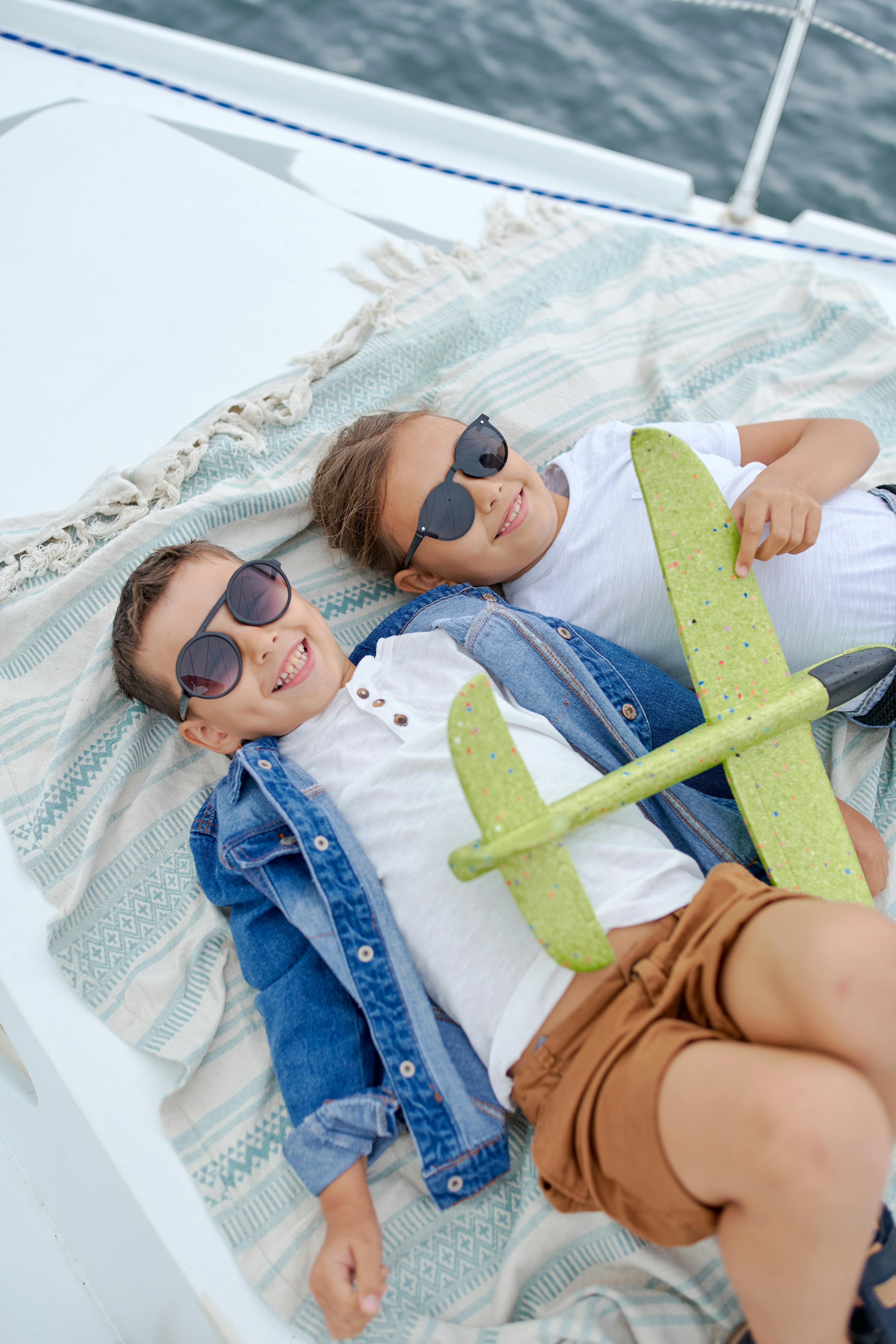Deux enfants heureux allongés face à face sur un bateau en train de jouer avec un avion jouet | Source : Pexels
