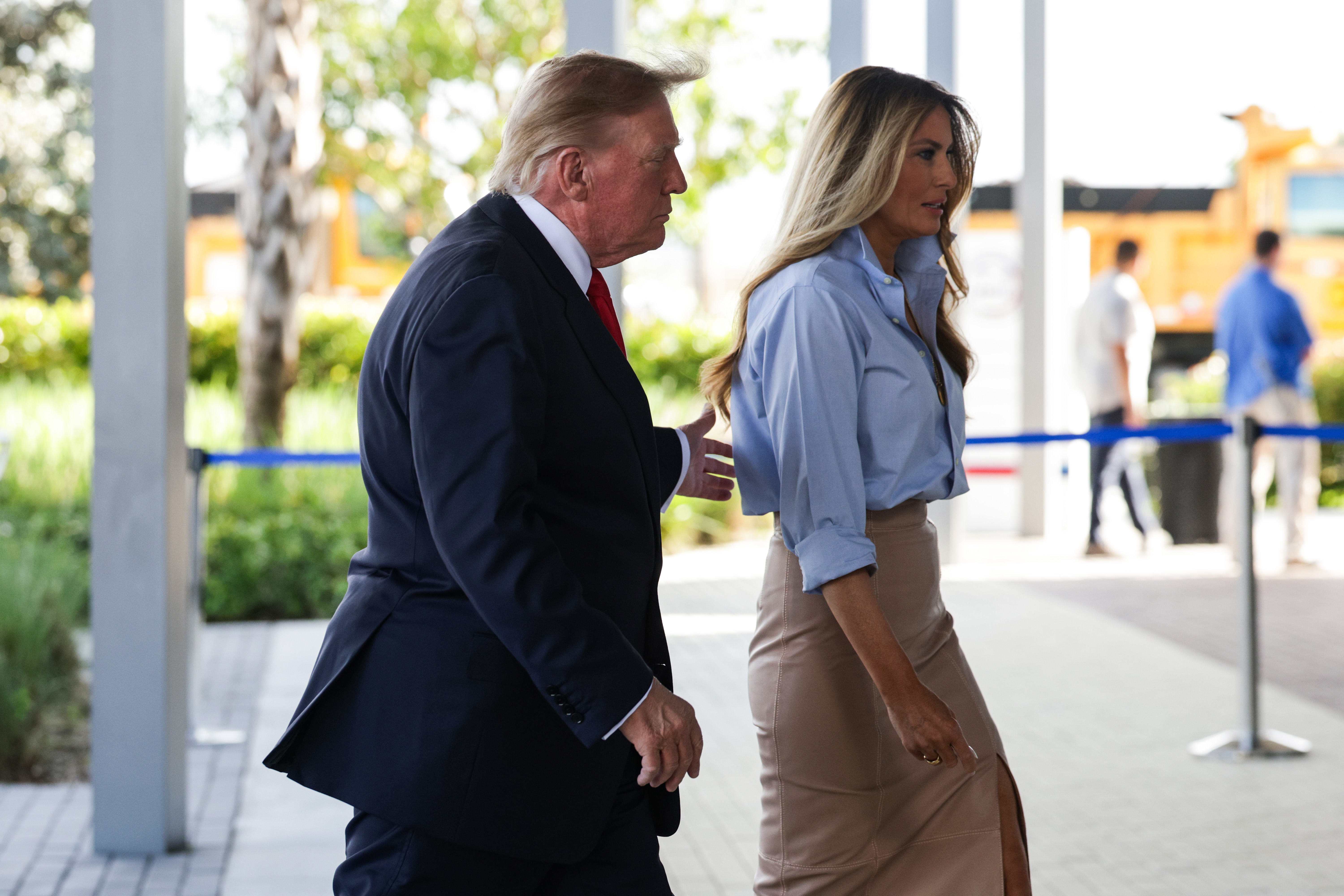 La Première Dame Melania Trump marche aux côtés du président Donald Trump devant les locaux du responsable des élections du comté de Palm Beach, à West Palm Beach, en Floride, le 24 octobre 2026, pour voter par anticipation aux élections de mi-mandat. Pour apporter une touche de structure décontractée à sa tenue de jour, elle associe une chemise bleu ciel déboutonnée et une jupe crayon fendue beige à taille haute à de vertigineuses chaussures à talons aiguilles nude à bout pointu qui allongent nettement sa démarche.