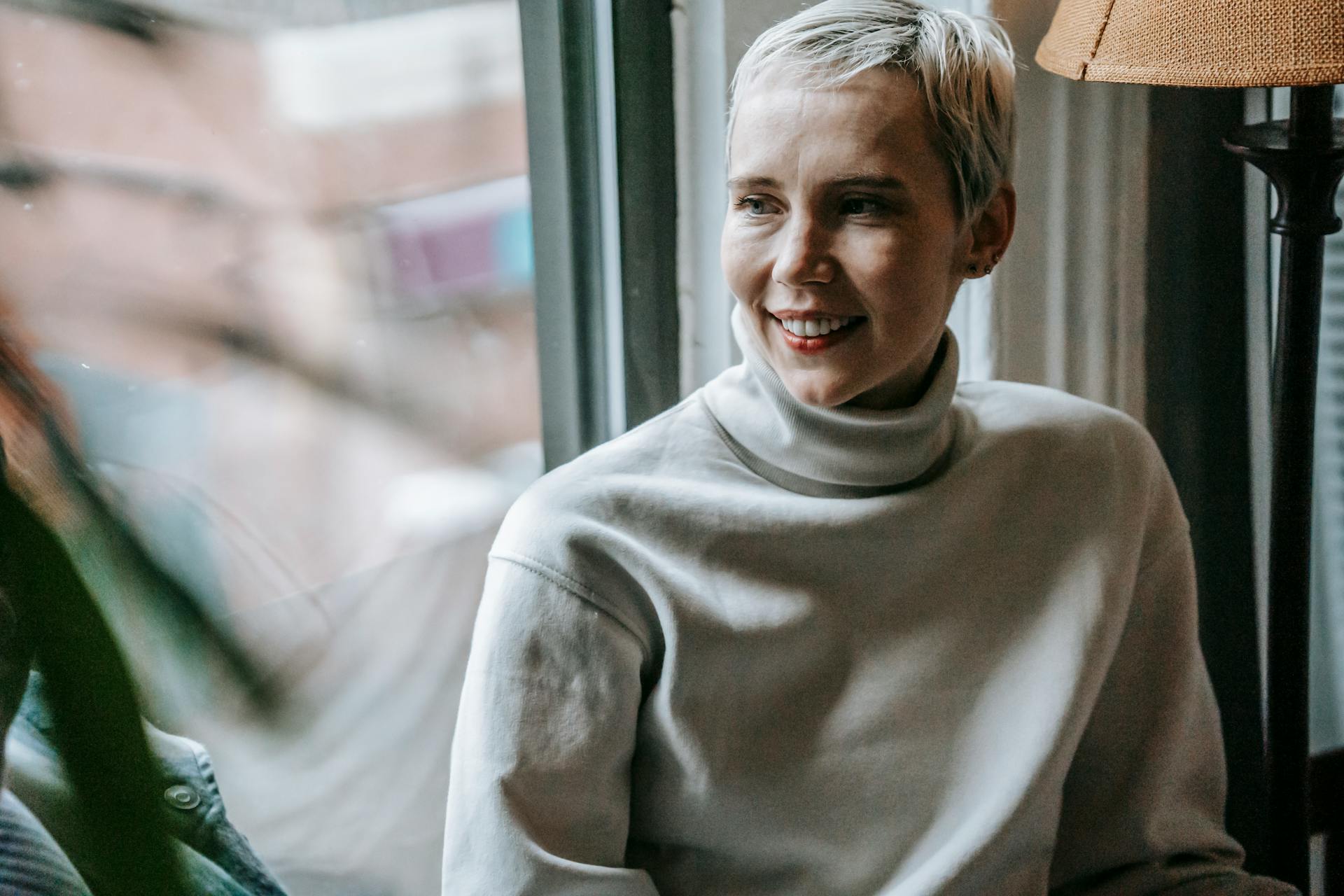 Une femme qui sourit en regardant par la fenêtre | Source : Pexels