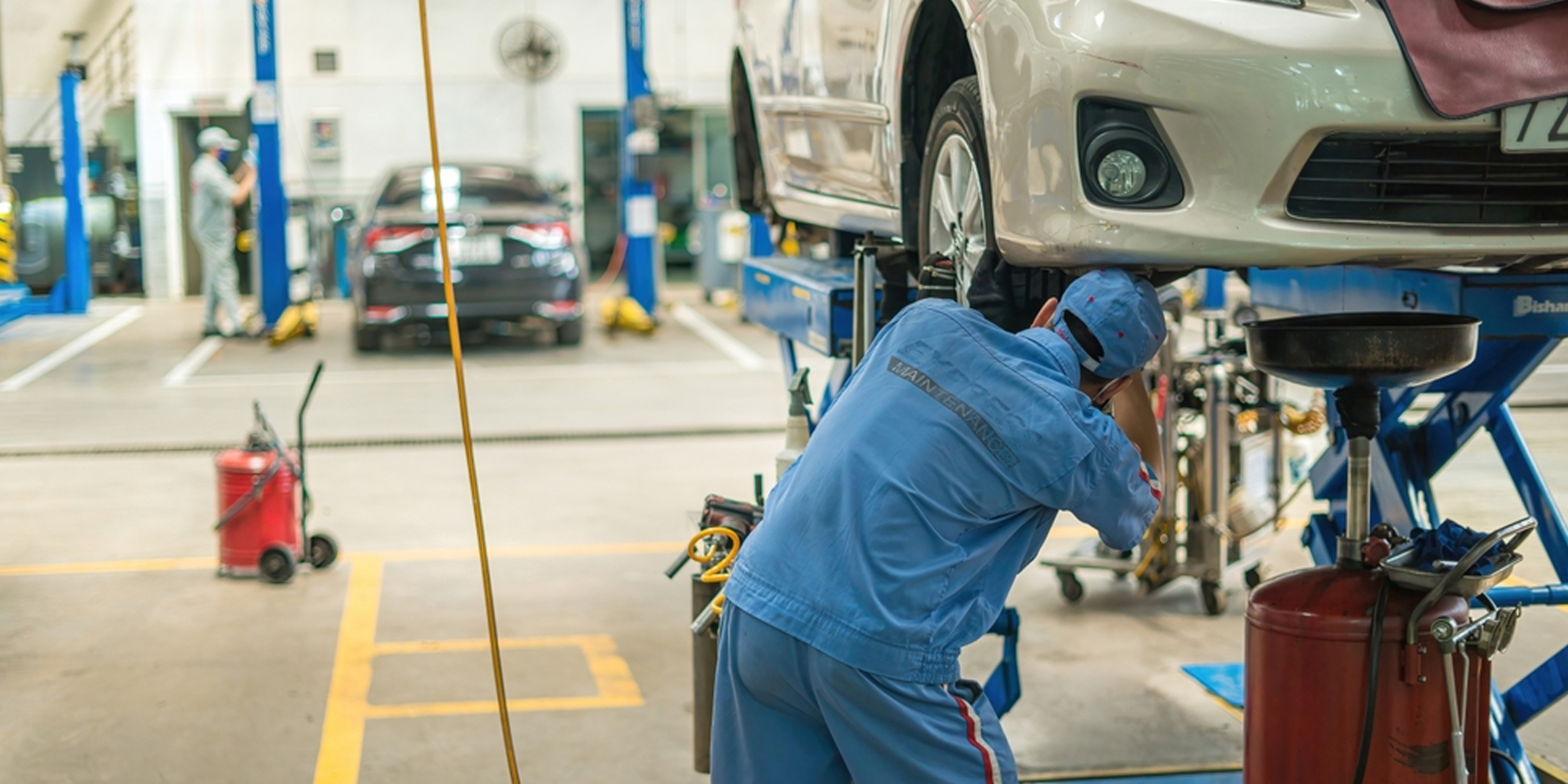 Un mécanicien travaille sous une voiture soulevée dans un atelier de réparation automobile très fréquenté | Source : Shutterstock