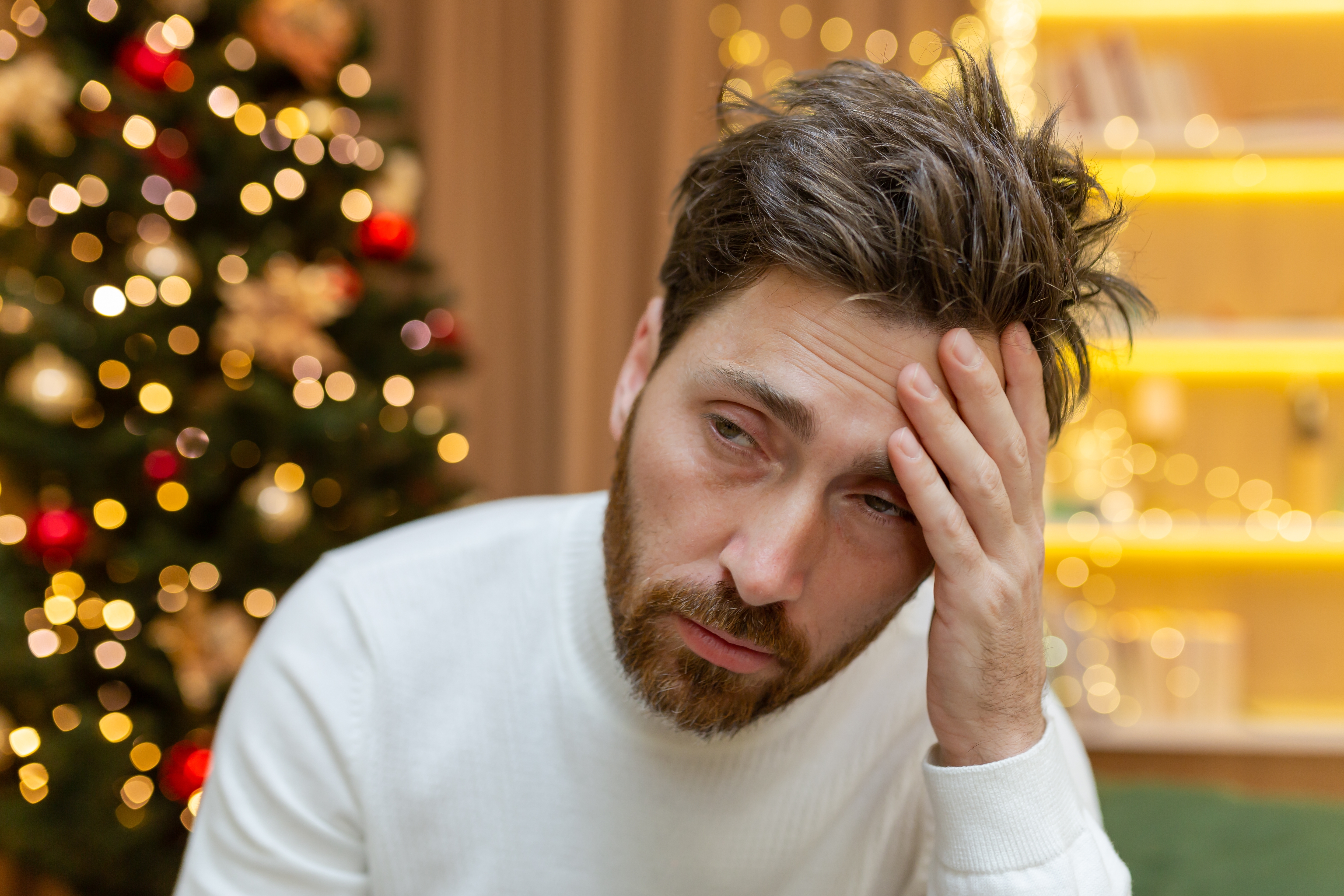 Un homme déprimé assis près d'un arbre de Noël à la maison | Source : Shutterstock