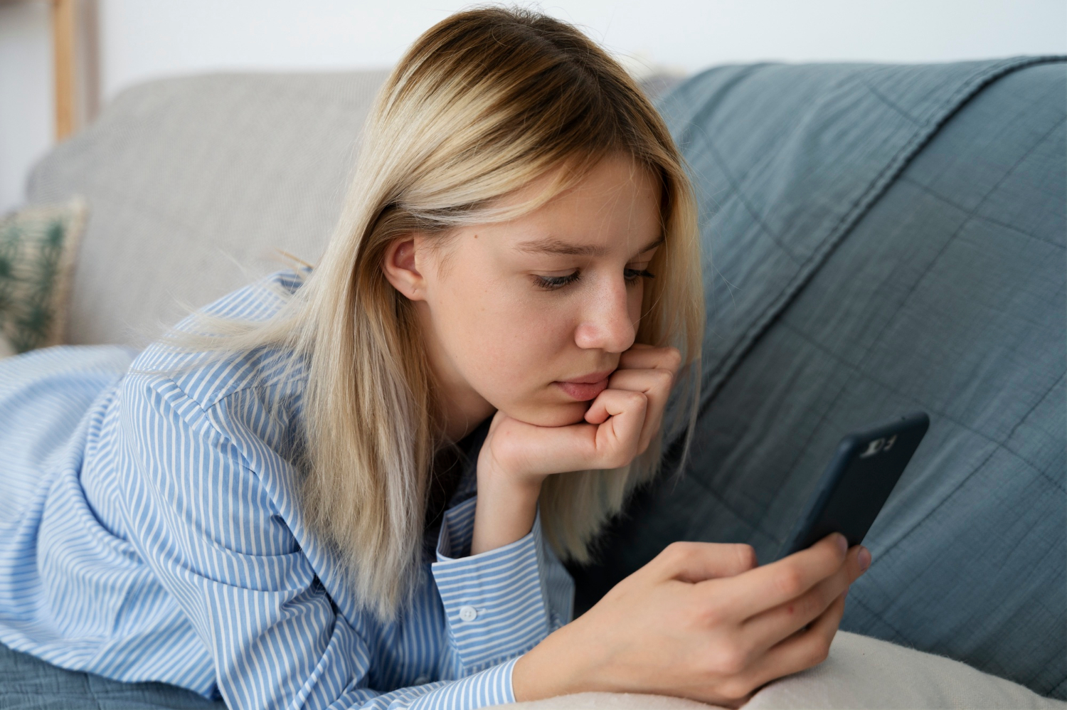 Une adolescente triste allongée sur le canapé et regardant son téléphone | Source : Freepik